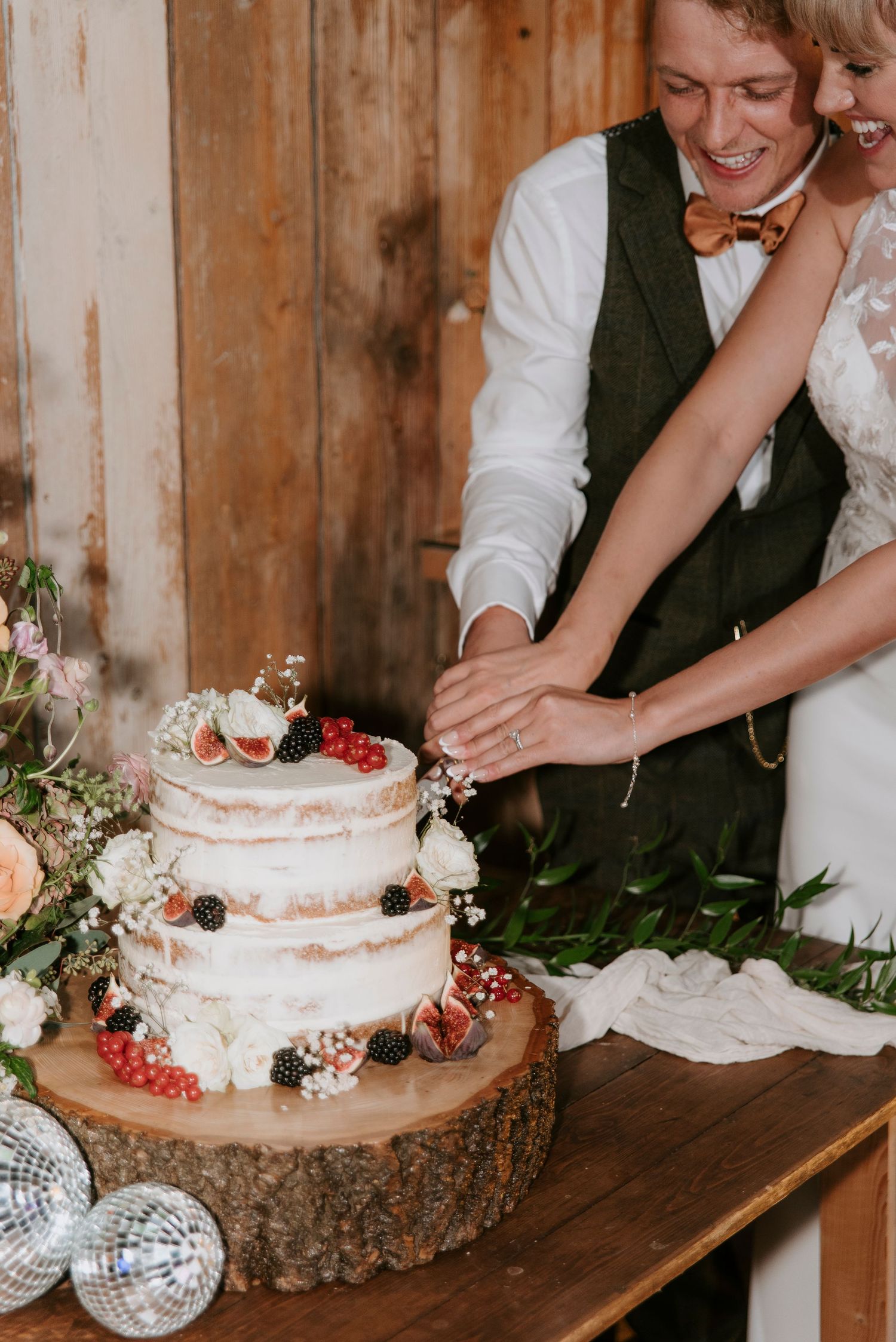 A rustic wedding cake cutting scene on a wooden slab with white frosting and red berries as decoration.