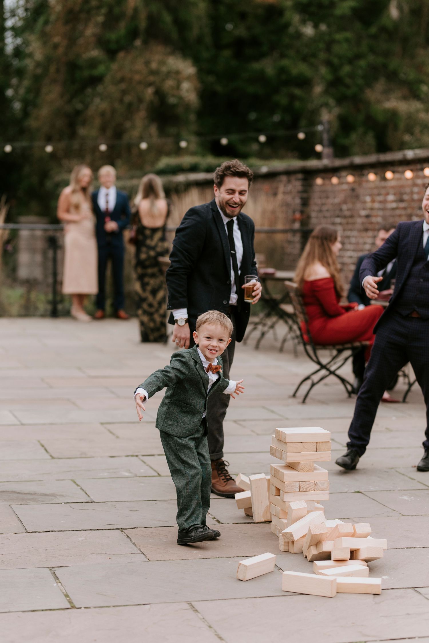 Young child in a green jacket plays with wooden blocks on a stone patio during an outdoor event.