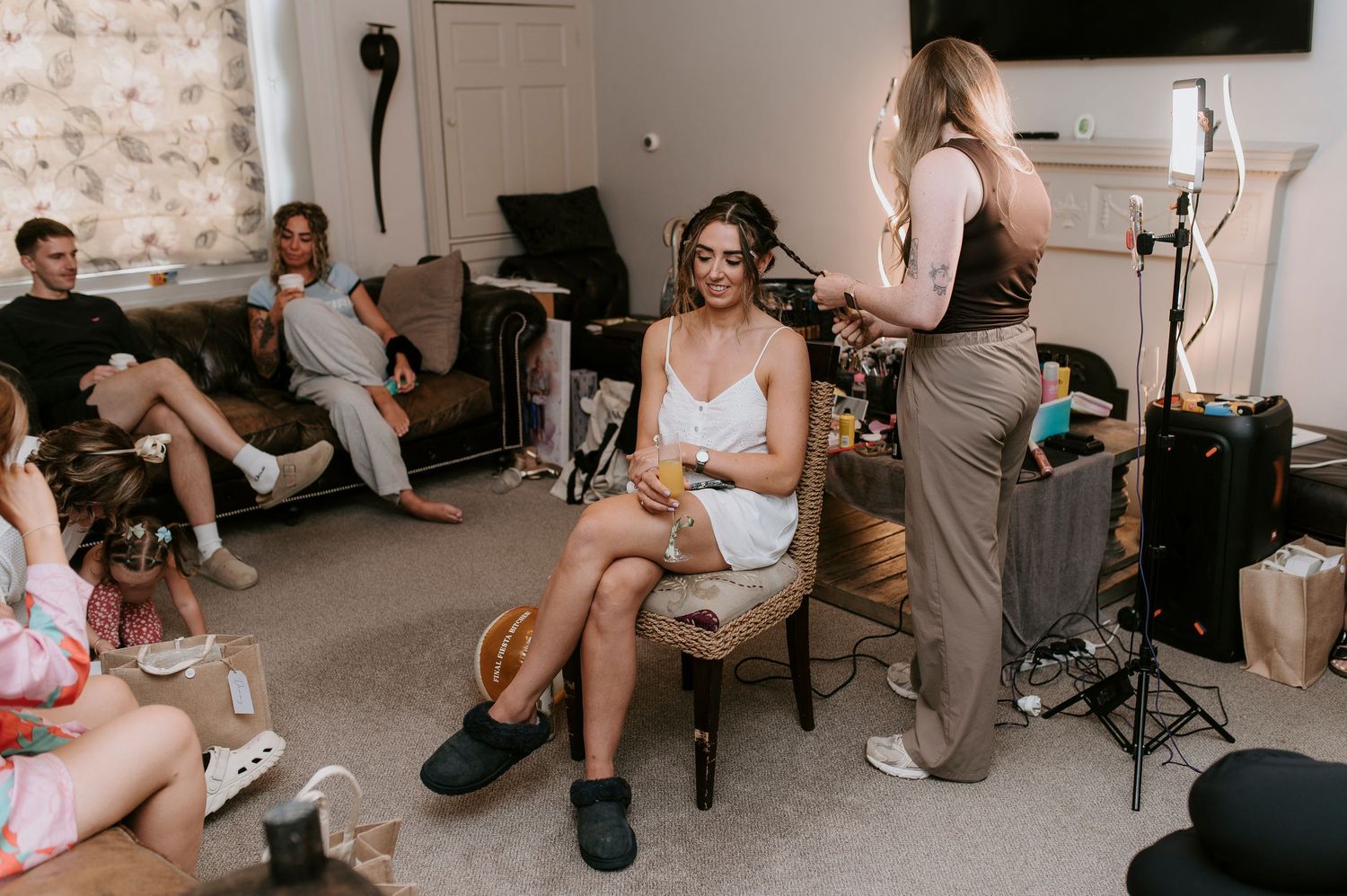 A casual gathering in a living room with people getting ready, featuring lighting equipment and comfortable seating.
