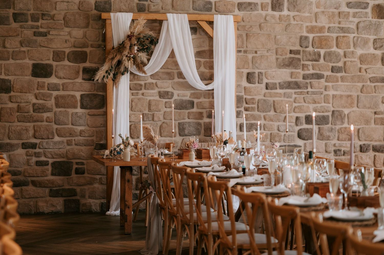 Rustic wedding reception venue with exposed brick walls, white drapes, and elegant table settings in warm lighting.