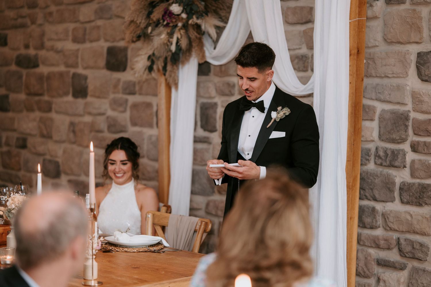 Stone wall interior of rustic wedding venue with white drapes and elegant table settings.