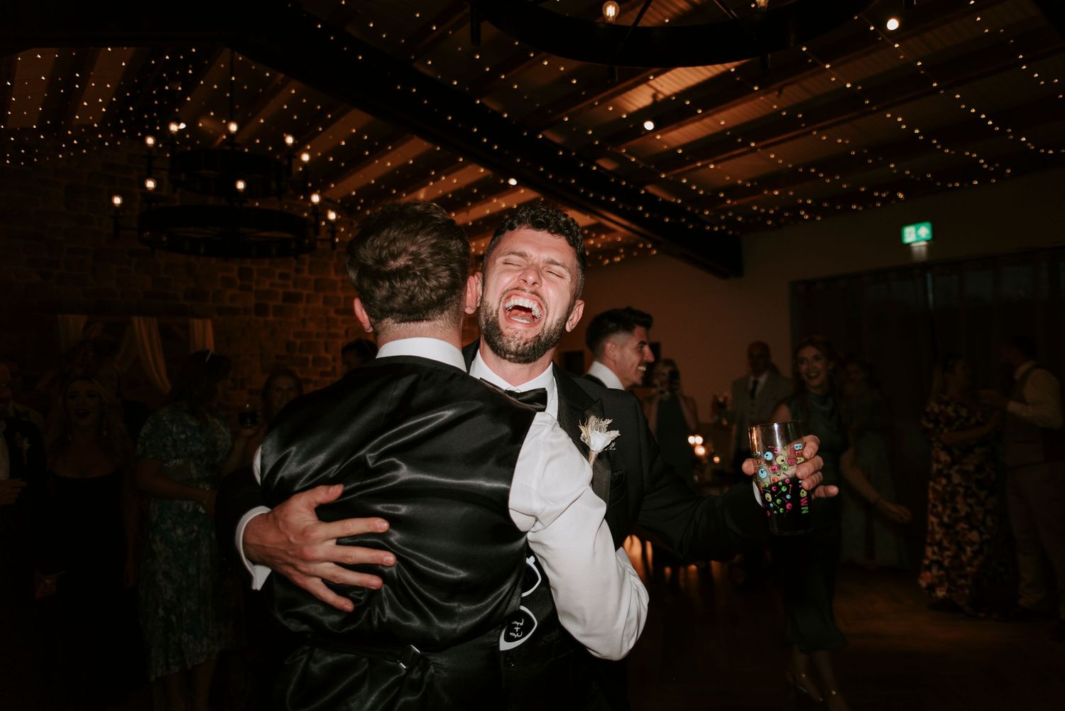 A couple shares an intimate dance moment at a wedding reception under twinkling lights.