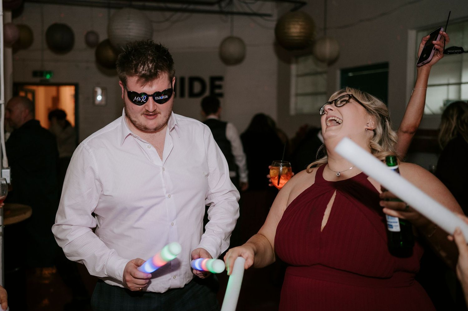 Two guests dance and celebrate with glow sticks at a lively wedding reception party.