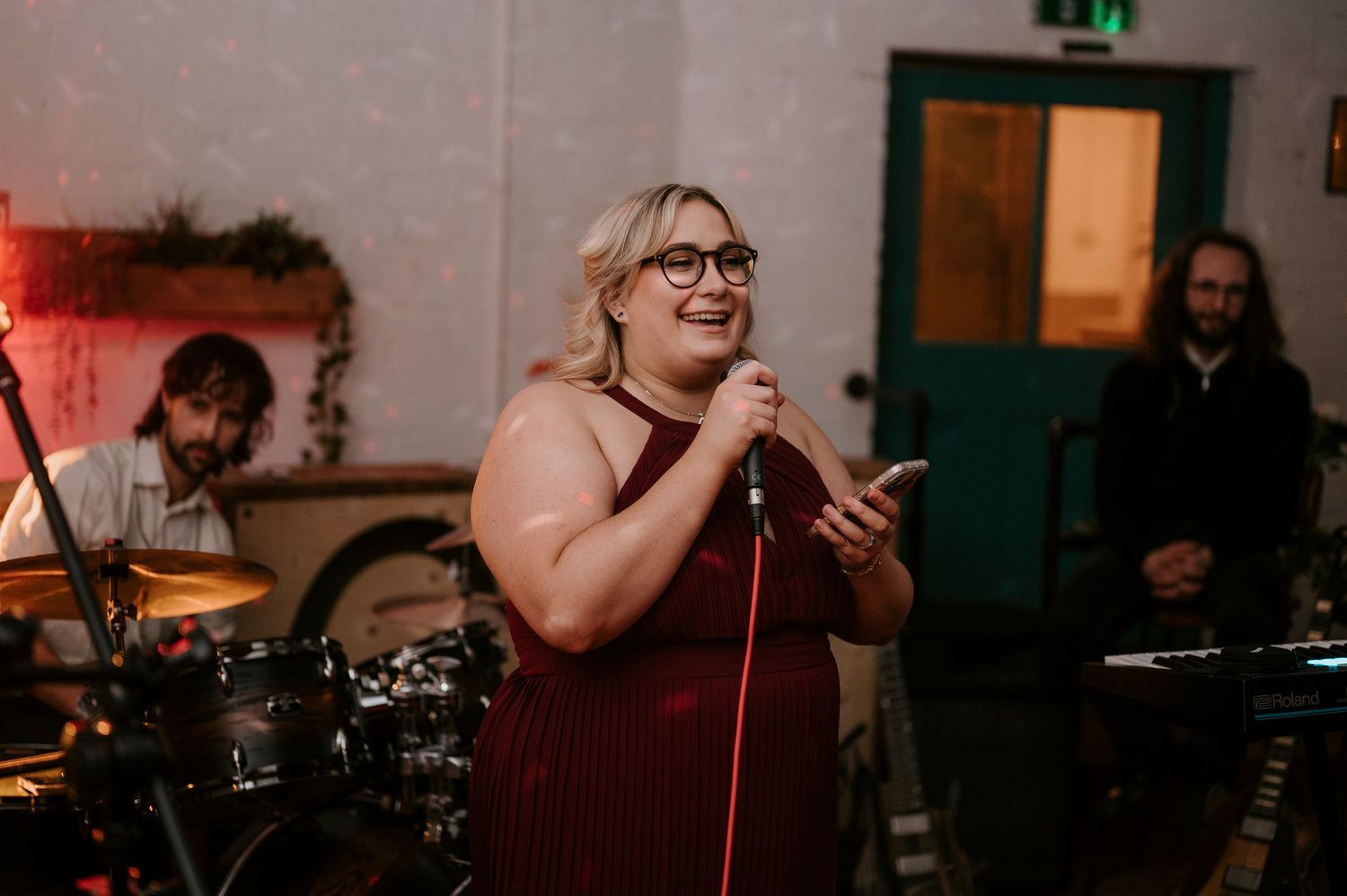Female singer performs at wedding reception holding microphone in elegant burgundy gown.