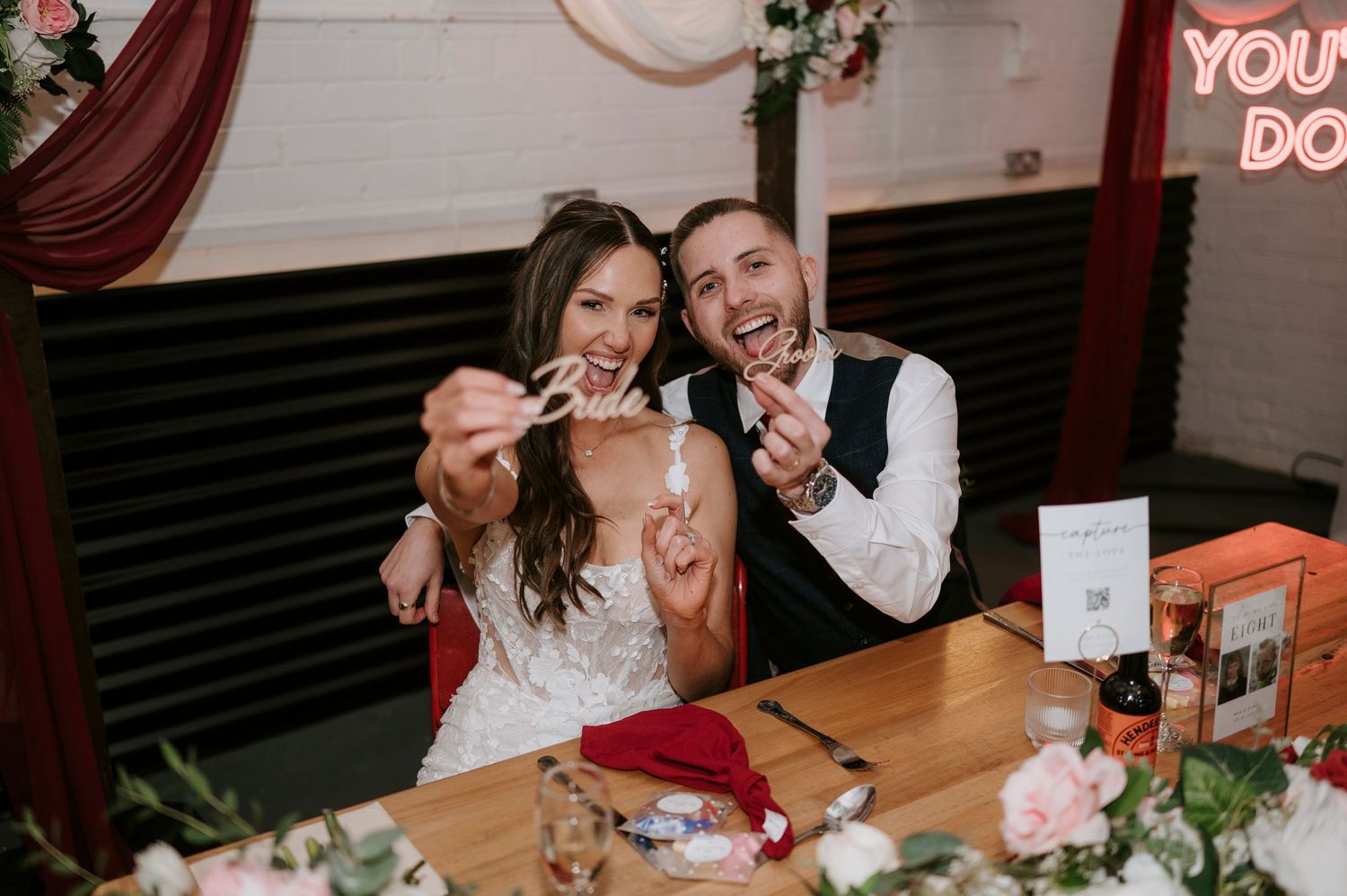 Bride and groom laughing together at sweetheart table during wedding reception.