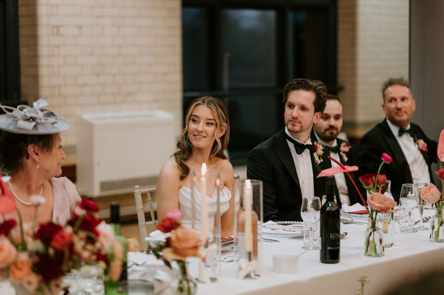 Wedding guests seated at an elegant reception dinner table with glowing candles and floral centerpieces.