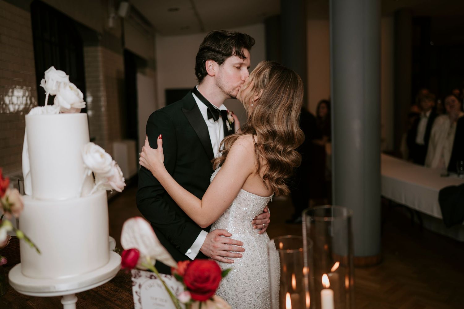 A white tiered wedding cake sits on a table surrounded by romantic candlelight and floral decorations.