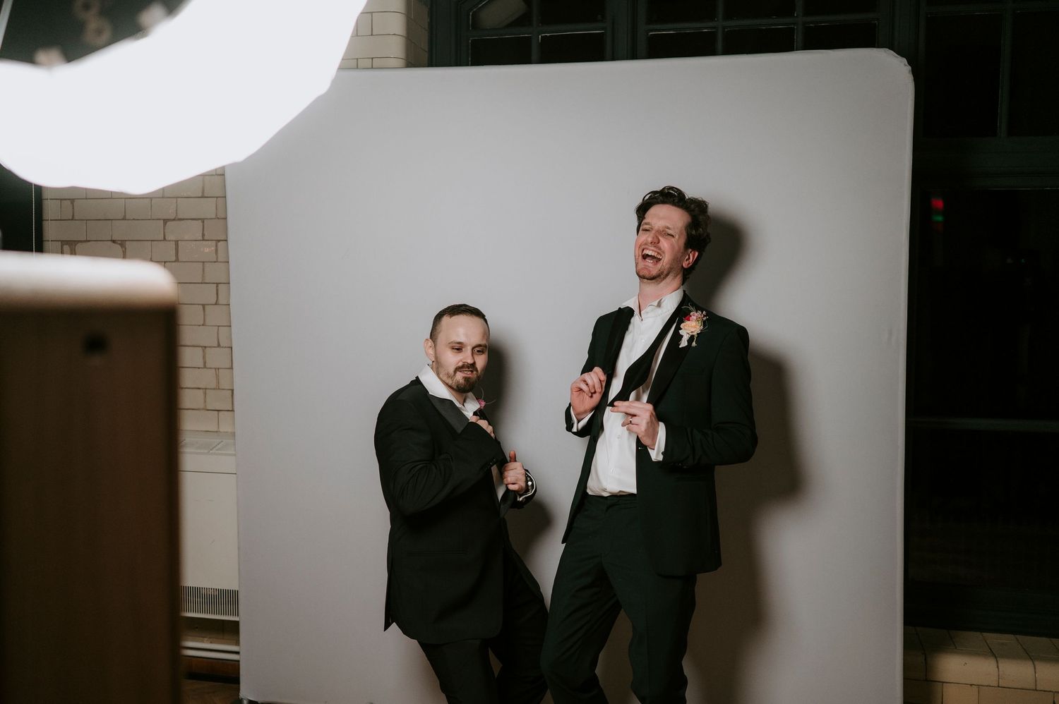 Two people in formal suits sharing a lighthearted moment against a white backdrop.