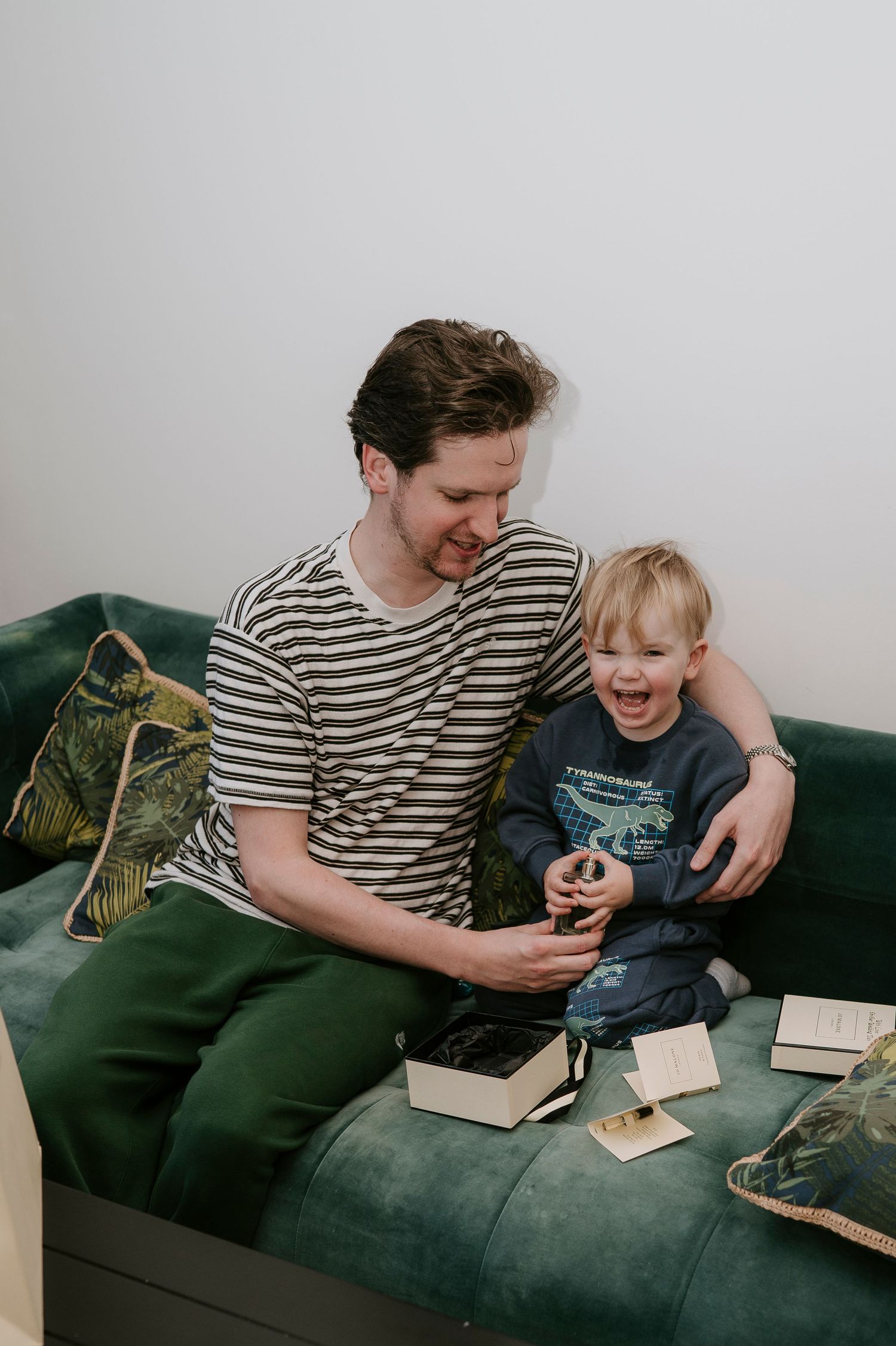 Parent and child share a lighthearted moment while reading together on a dark green couch.