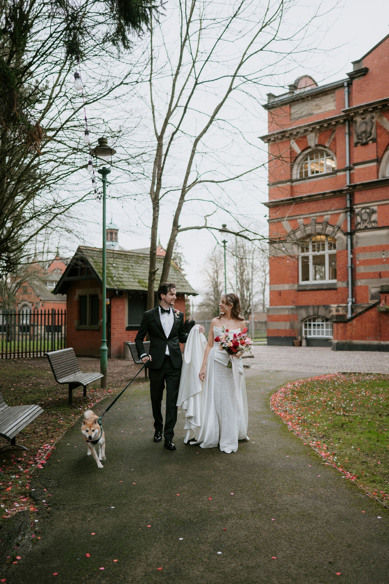 Wedding couple walking through autumn grounds of brick building with fallen leaves.