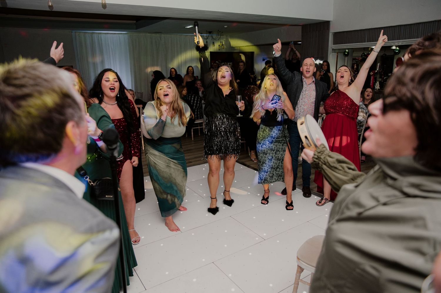 A group of people dancing and celebrating together in what appears to be a school hallway or community center.