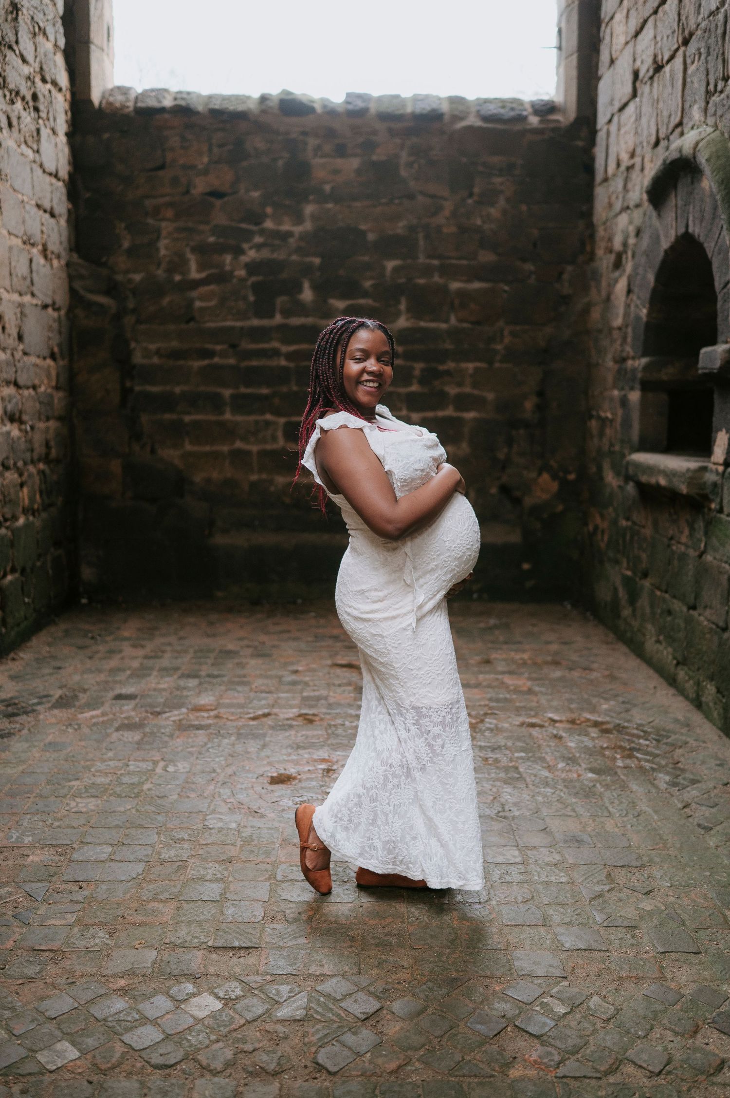 A person in a white lace wedding dress poses gracefully against stone walls in a historic building.