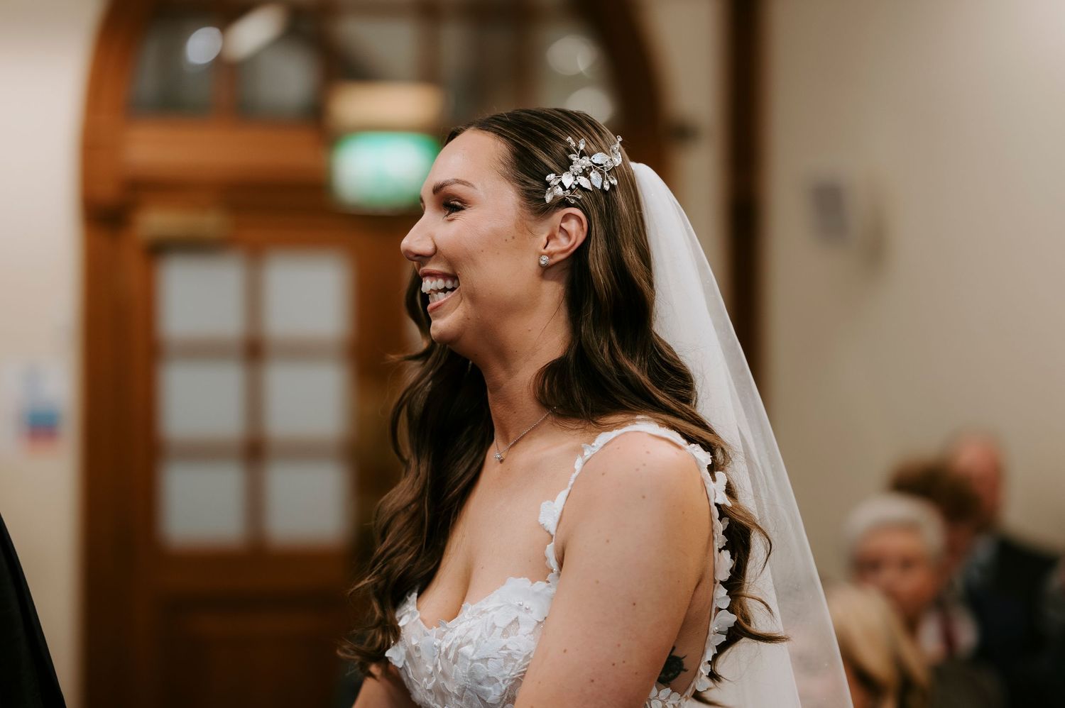 Smiling bride in lace wedding dress and veil with floral hair accessory laughing joyfully during wedding ceremony.