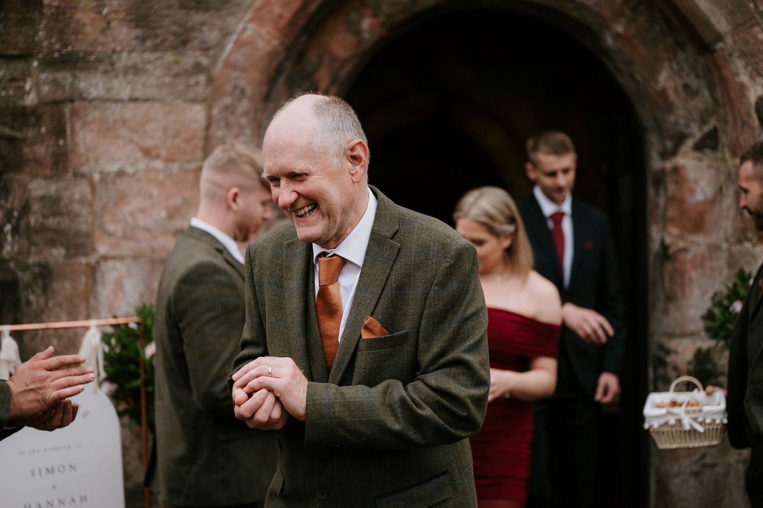 A wedding party celebrates with laughter and joy against a rustic brick wall backdrop at an elegant reception.