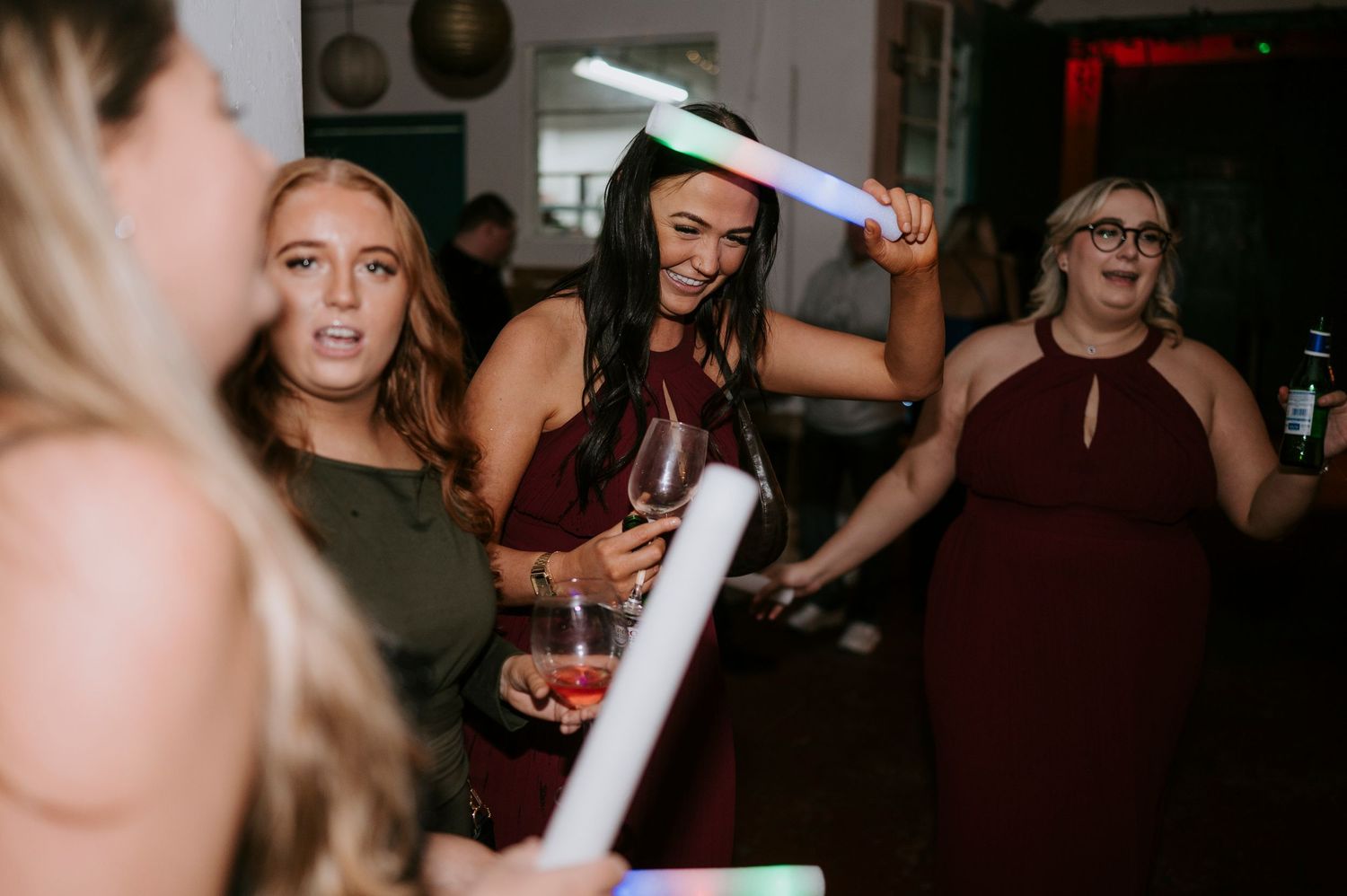 Women dancing and holding glow sticks at a wedding reception party.