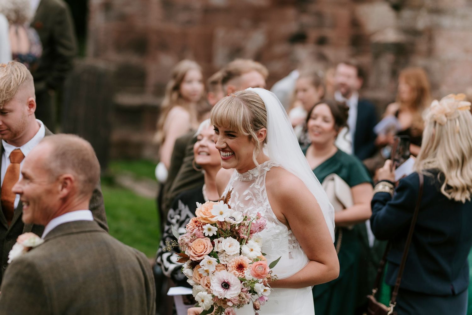 Wedding guests laugh and celebrate during an outdoor reception at a historic stone building venue.