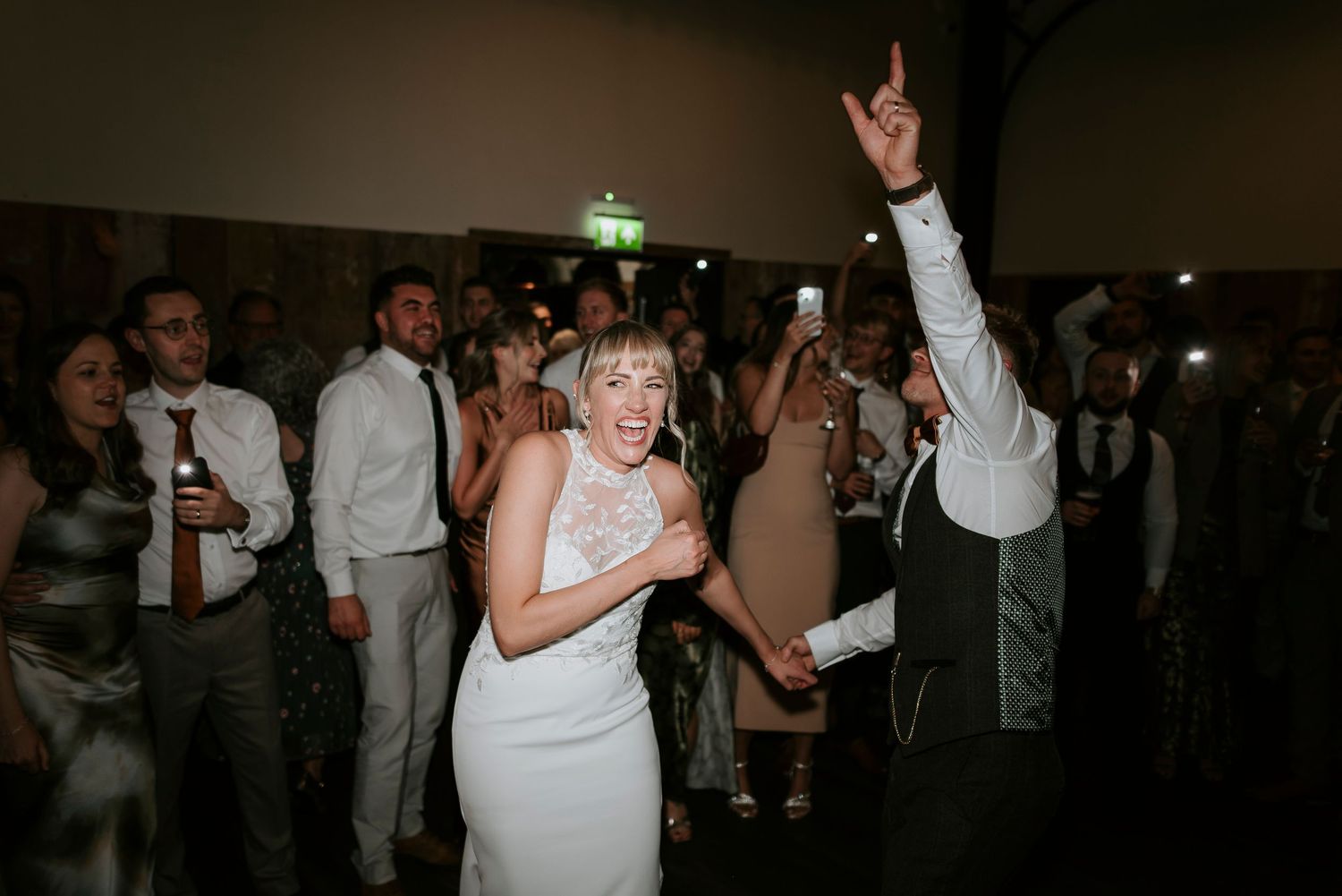 Wedding guests dance and celebrate on a dark dance floor during a reception party.