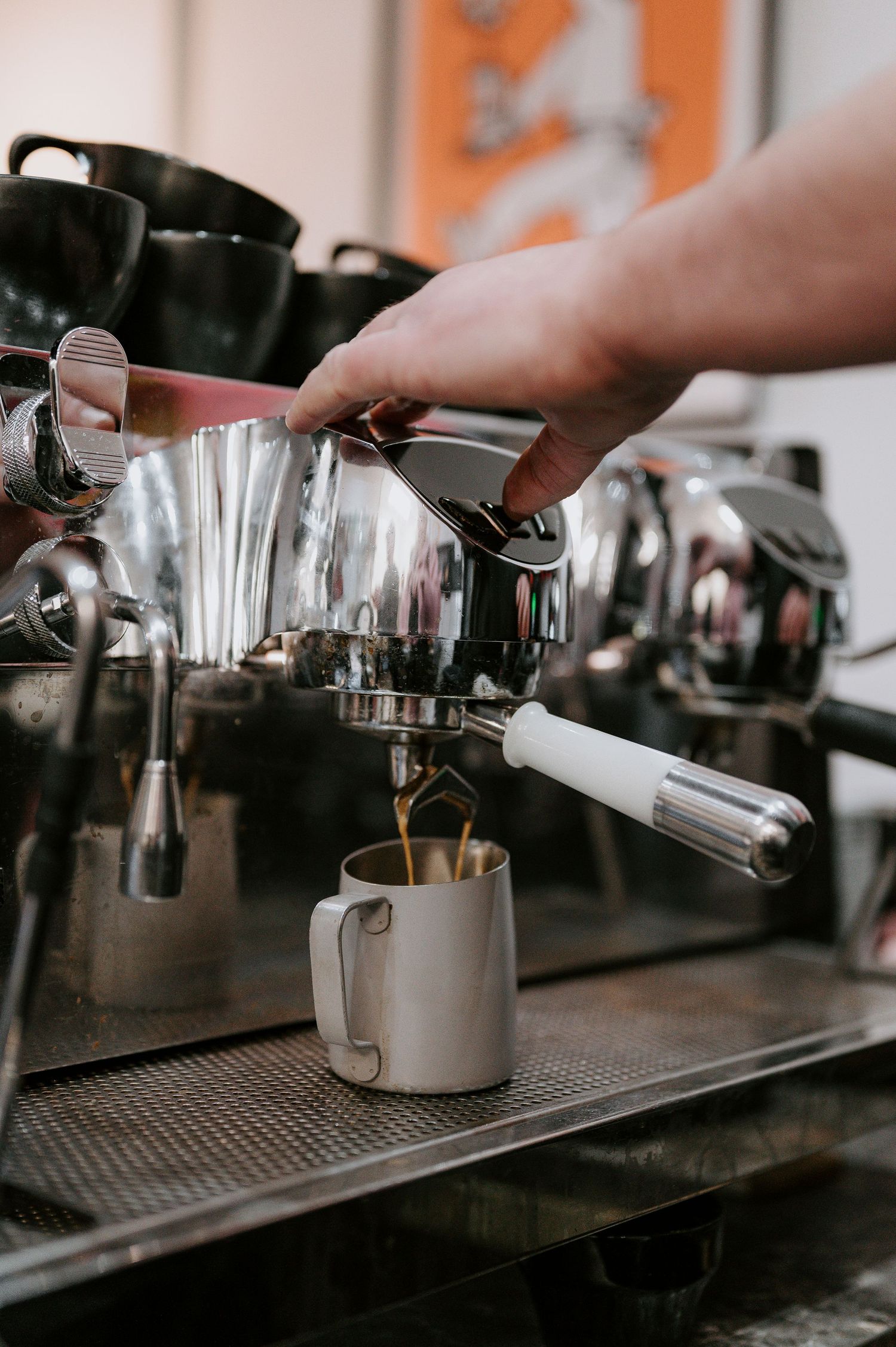 Barista steaming milk in metal pitcher on professional espresso machine counter.