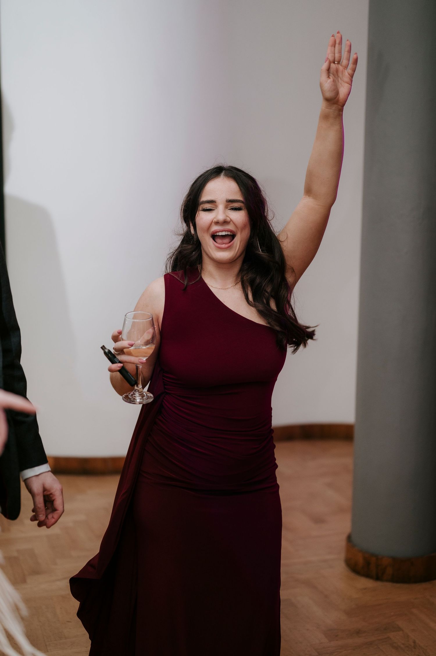 A guest in a burgundy dress celebrates enthusiastically on the dance floor at a wedding reception.