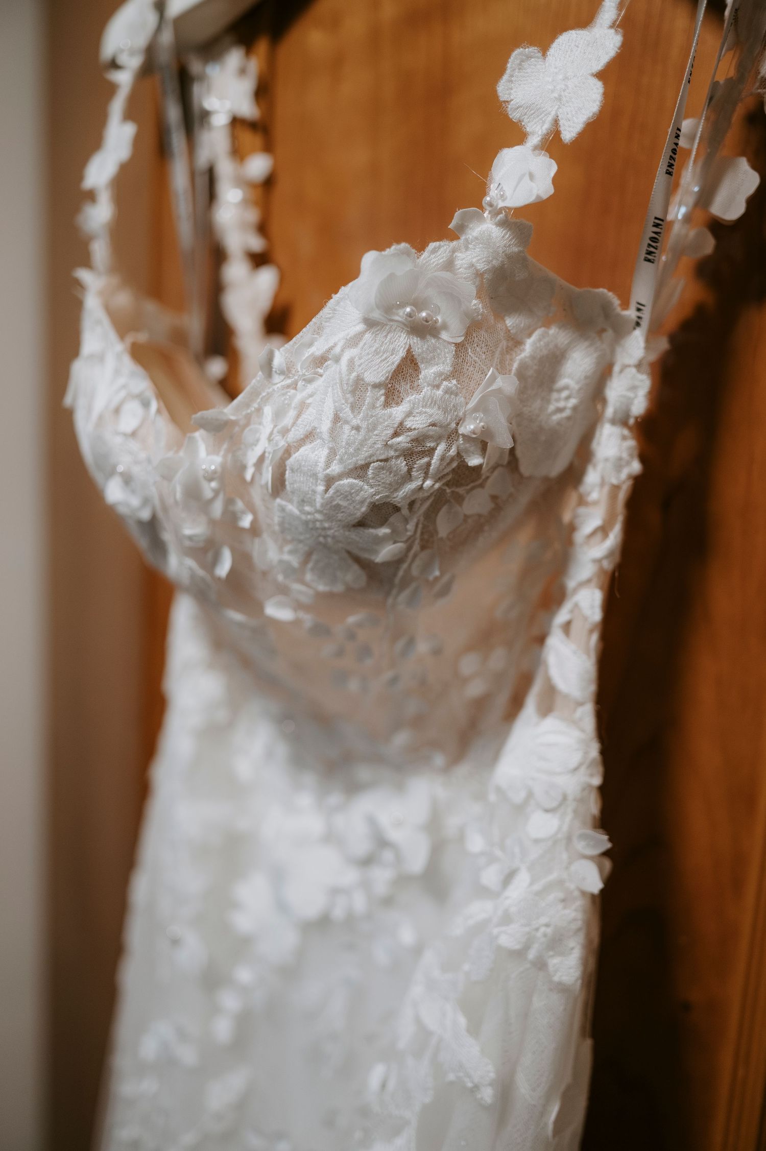 Close-up detail of a white wedding dress bodice with delicate lace appliques and beading against a wooden background.