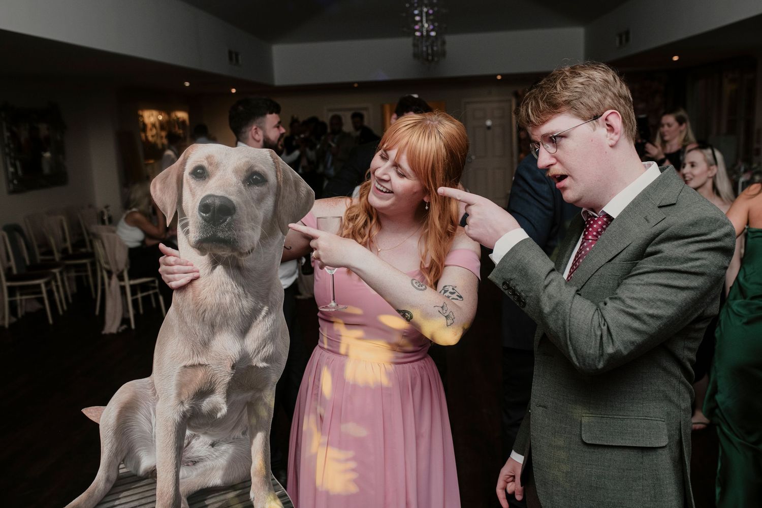 A couple dances with their dog at a wedding reception while other guests look on in the background.