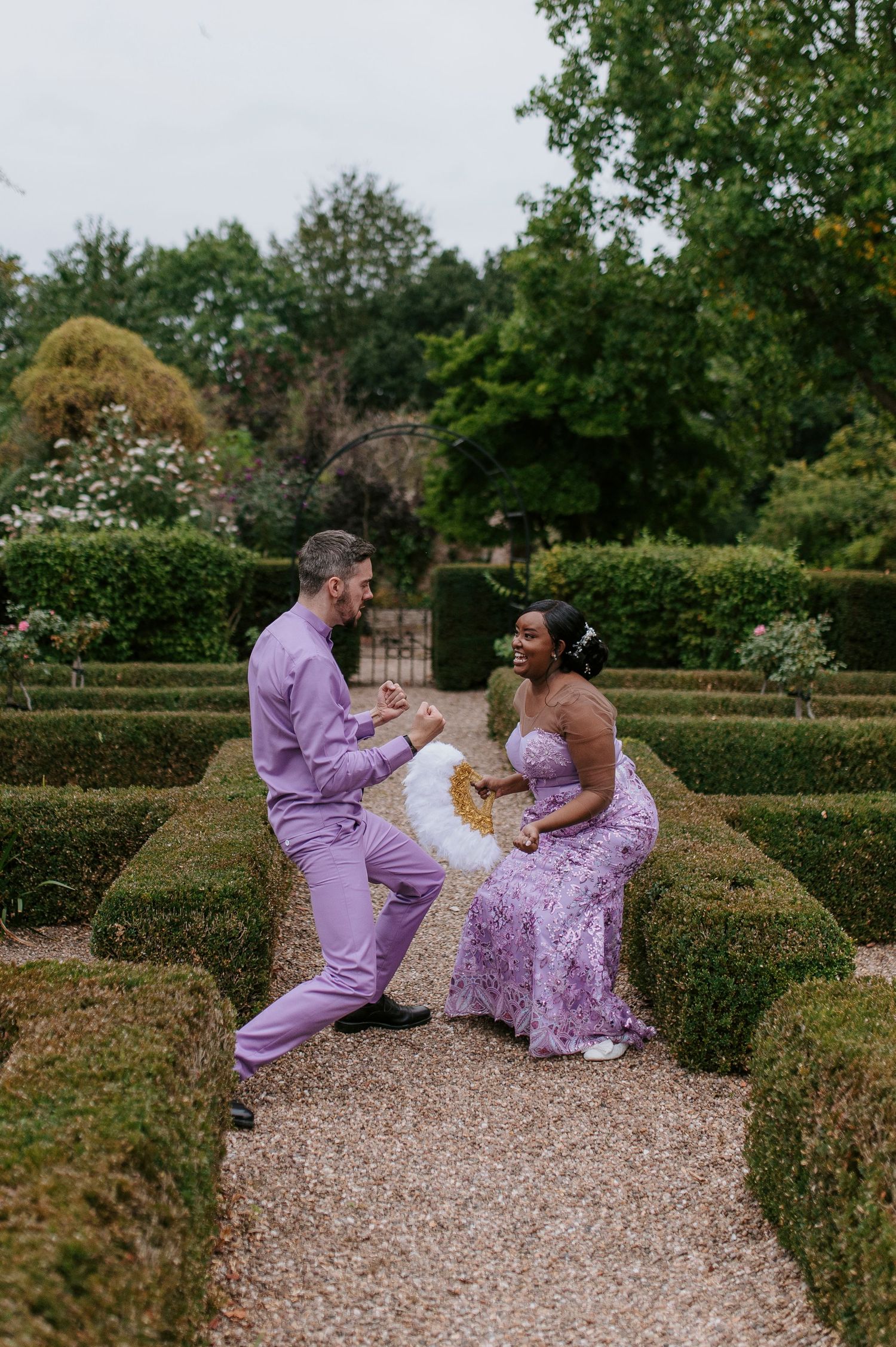 A family sits together on a gravel path surrounded by manicured hedges in a garden maze wearing coordinating purple outfits.