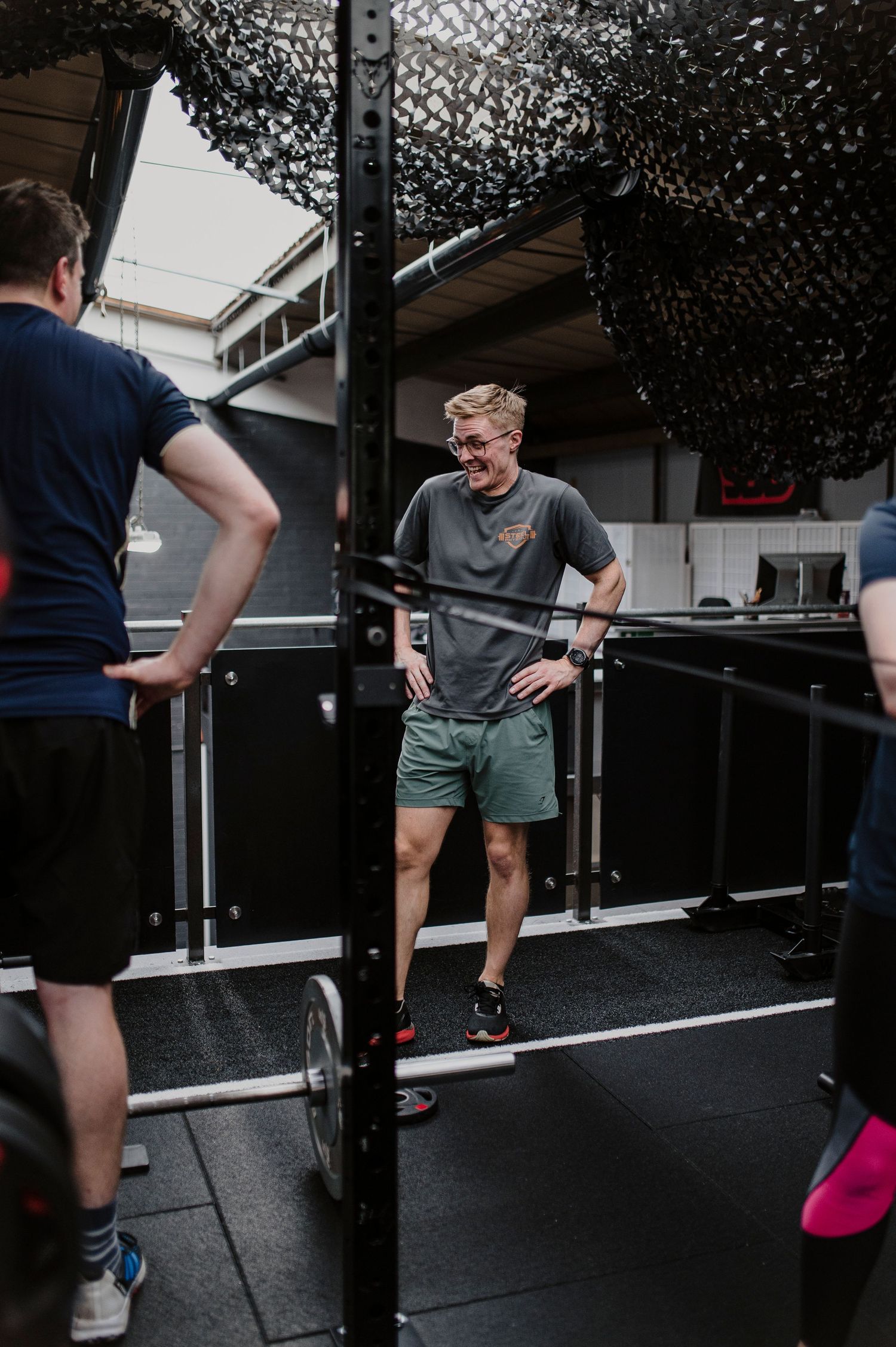 People exercising and training at an indoor gym facility with fitness equipment and black netting overhead.