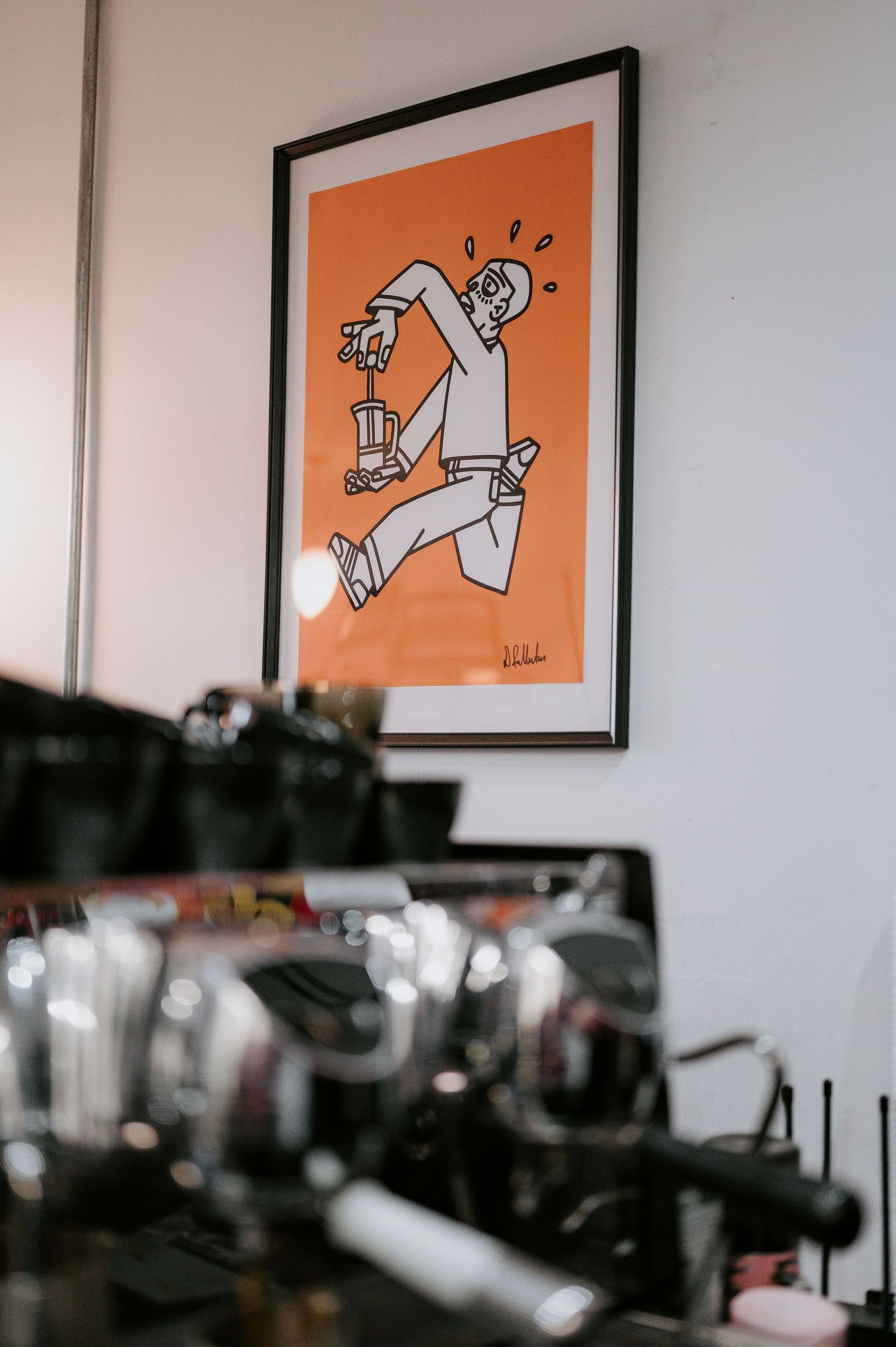 Orange and white minimalist cartoon art prints displayed on a white wall above coffee equipment.