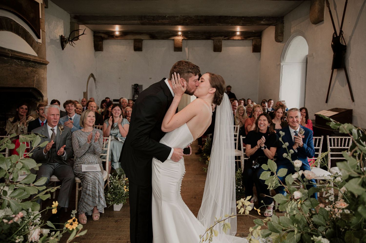 Indoor wedding ceremony with exposed beams and greenery decorations.