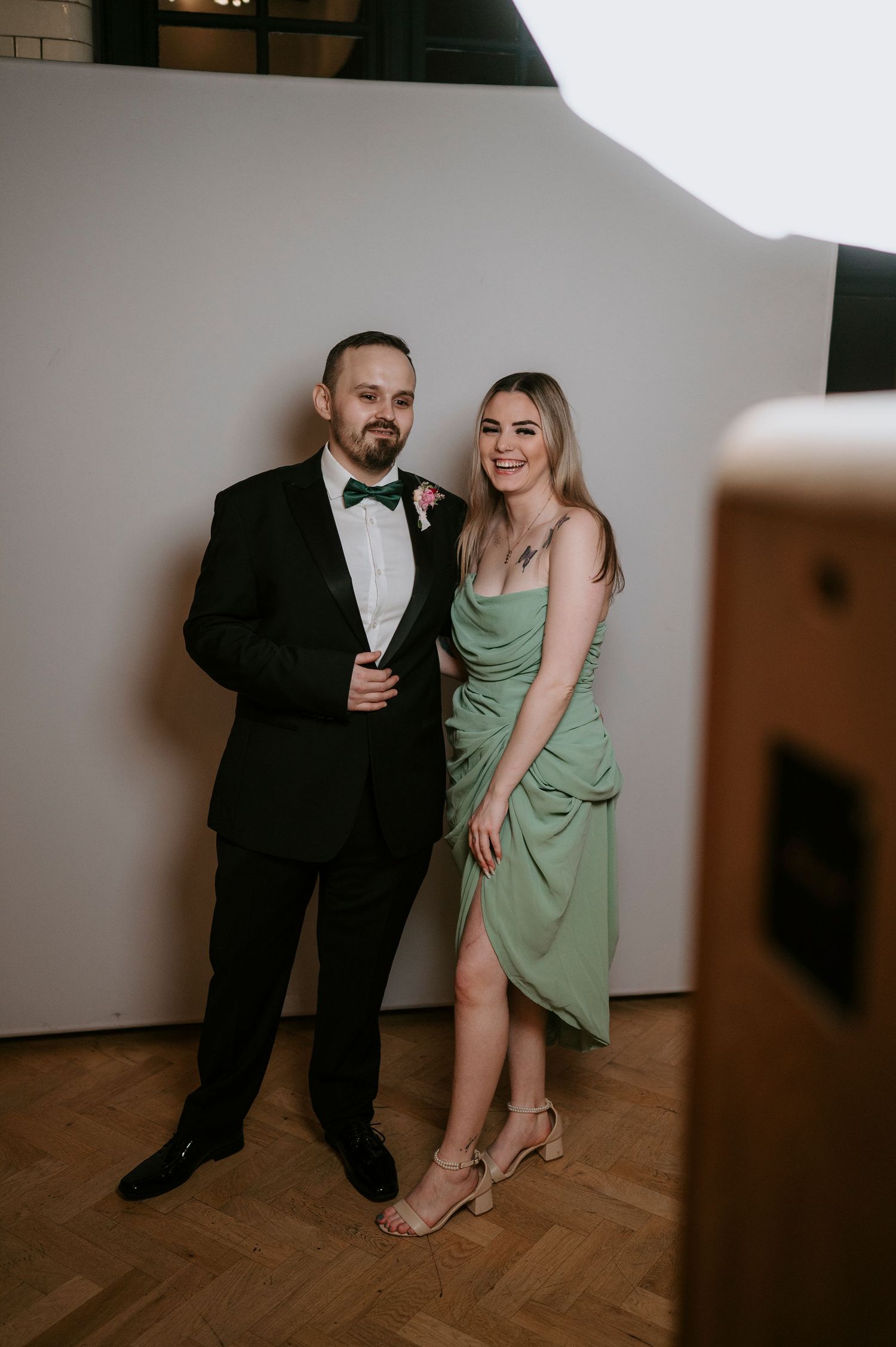 Couple in formal attire posing together on wooden floor during celebration.