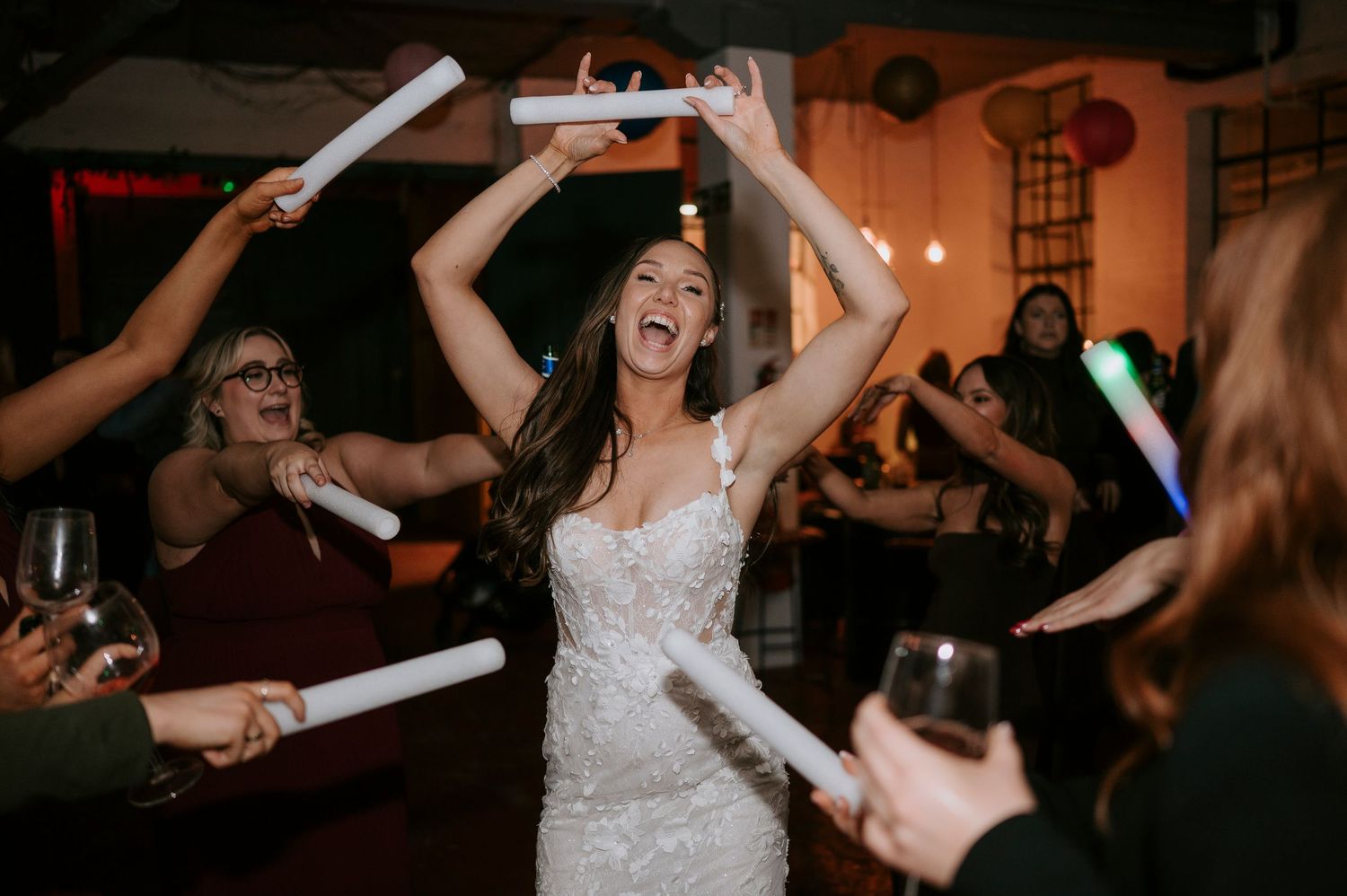 Joyful bride dancing with glowsticks raised above head surrounded by celebrating wedding guests.