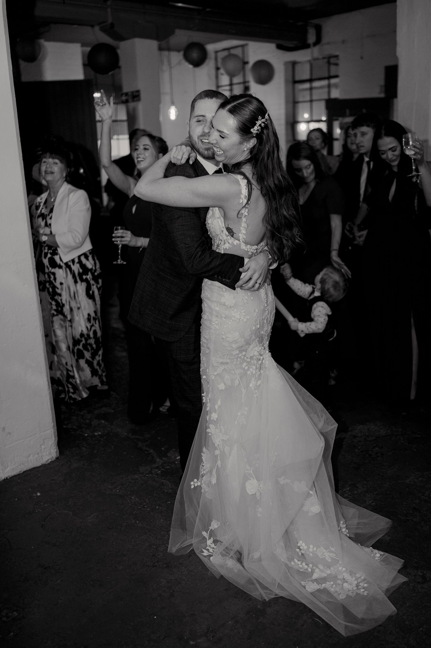 Bride and groom share first dance embrace in black and white wedding reception photo.