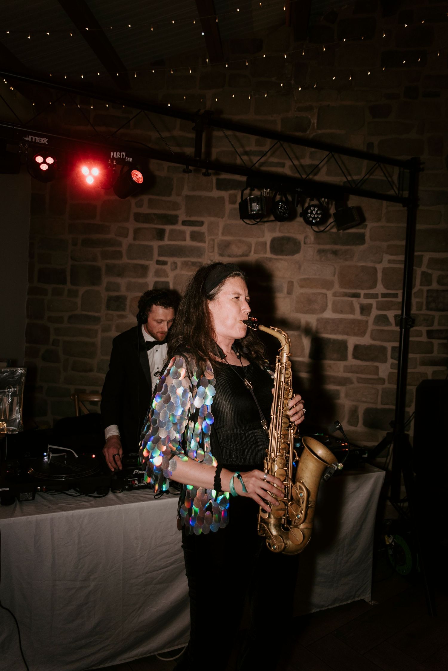 A saxophonist performs at a dimly lit venue with stone walls and atmospheric red lighting in the background.