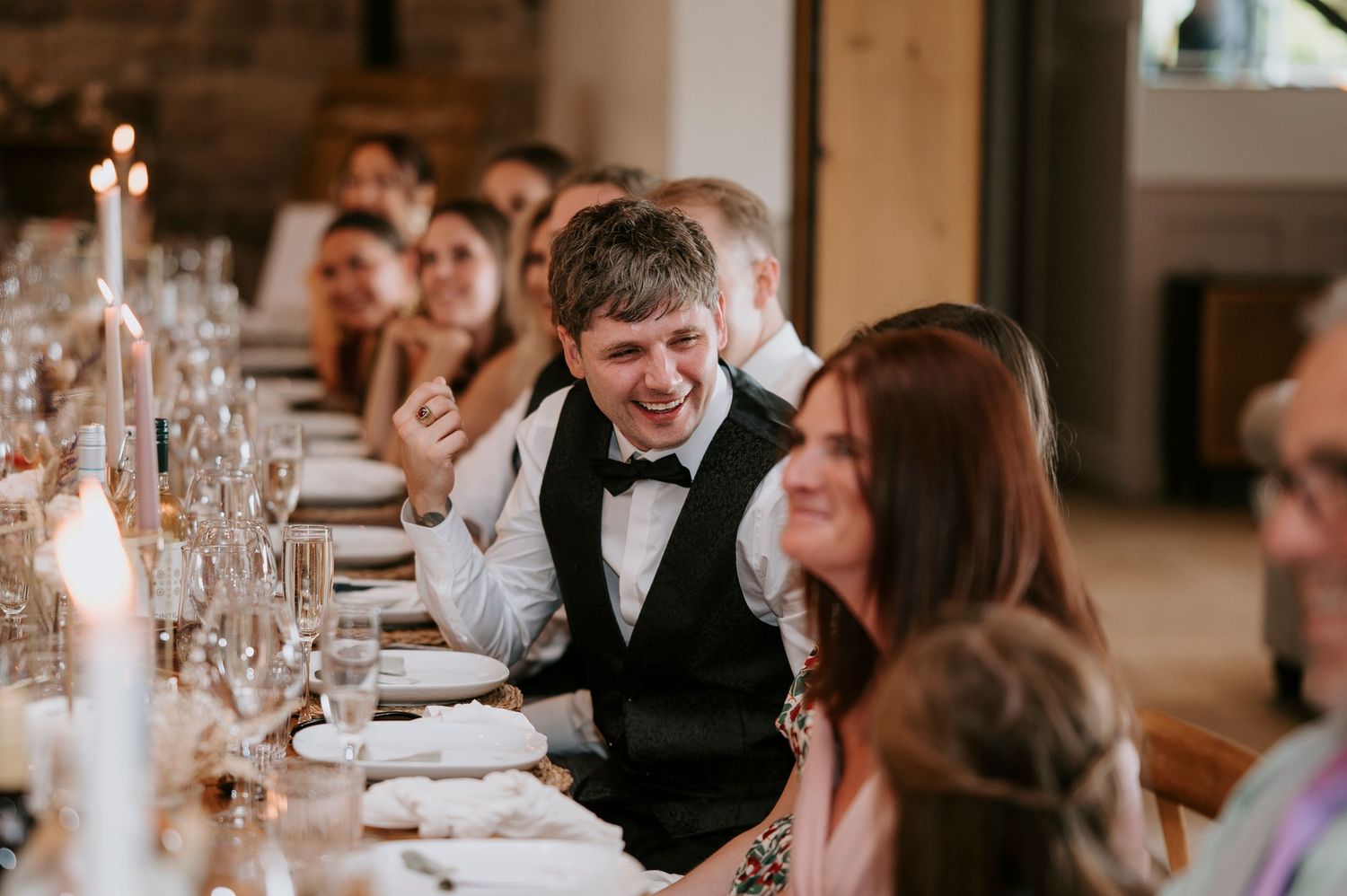 Wedding guests enjoy a candlelit dinner reception with elegant table settings and glowing ambiance.