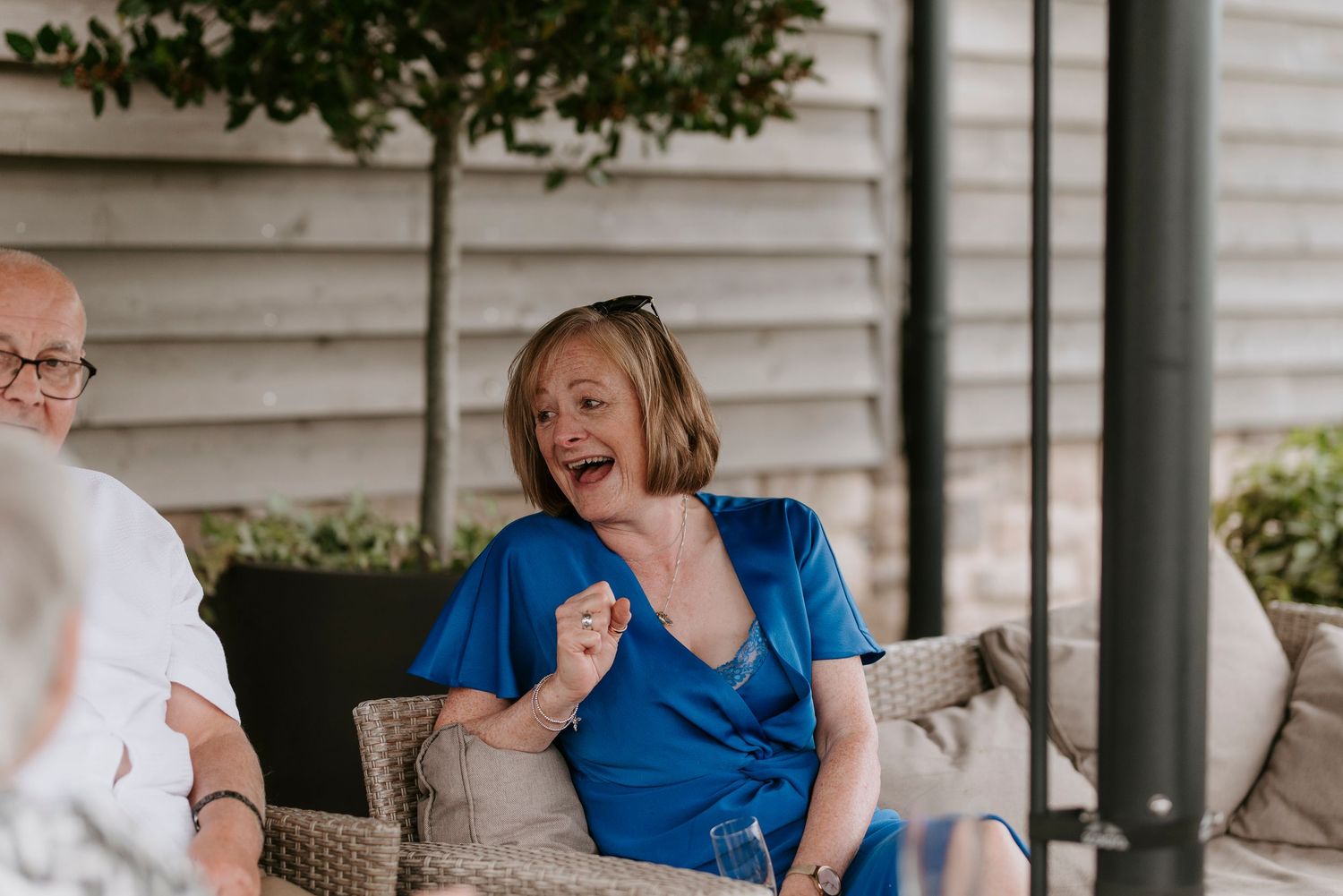A group of people sit and laugh together on an outdoor porch during a social gathering.