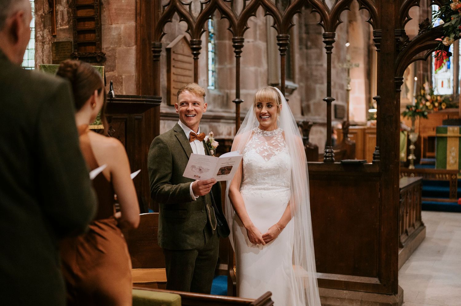 A wedding ceremony takes place inside a beautiful historic church with ornate wooden details and stained glass windows.