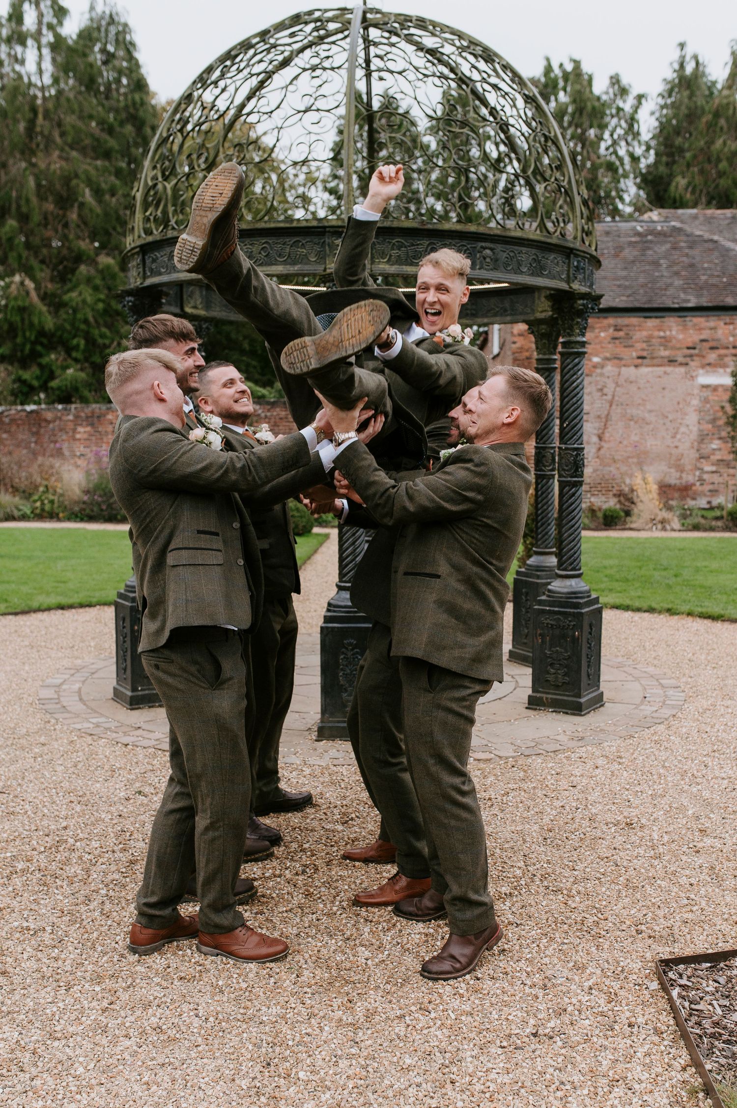 Two groomsmen in olive green suits playfully pose for a series of fun photos during a wedding celebration.