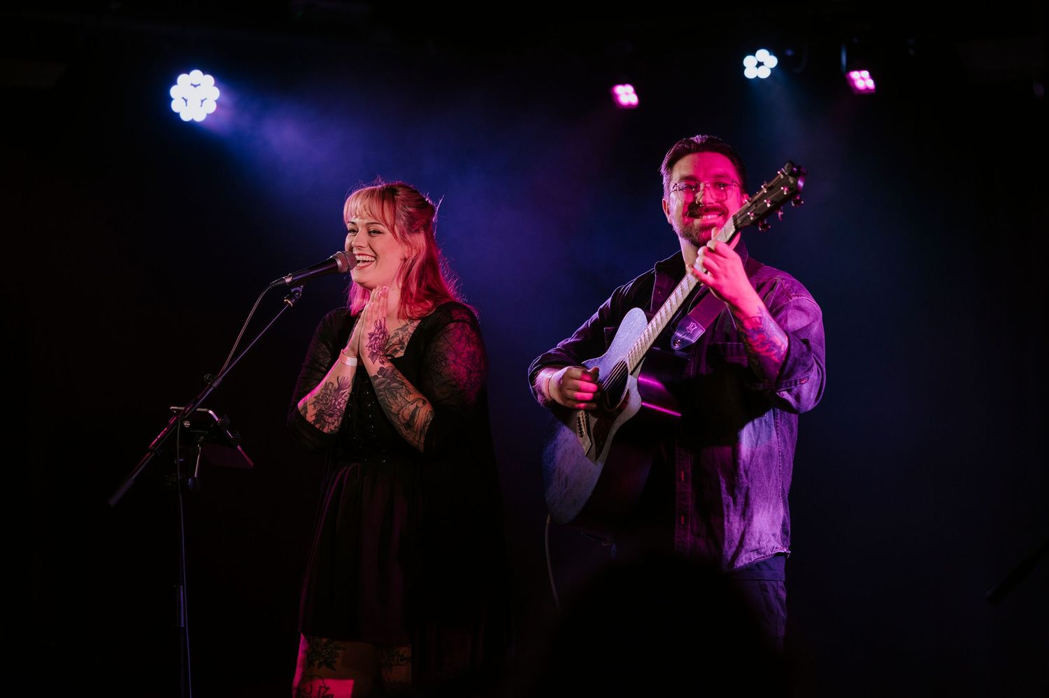 Musicians perform on stage under dramatic purple and blue lighting during a live concert performance.