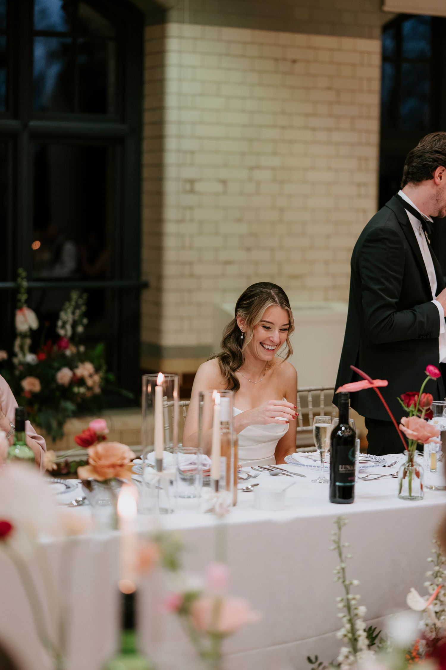 Formal dinner reception with white tablecloths and red floral arrangements in an elegant brick-walled venue.