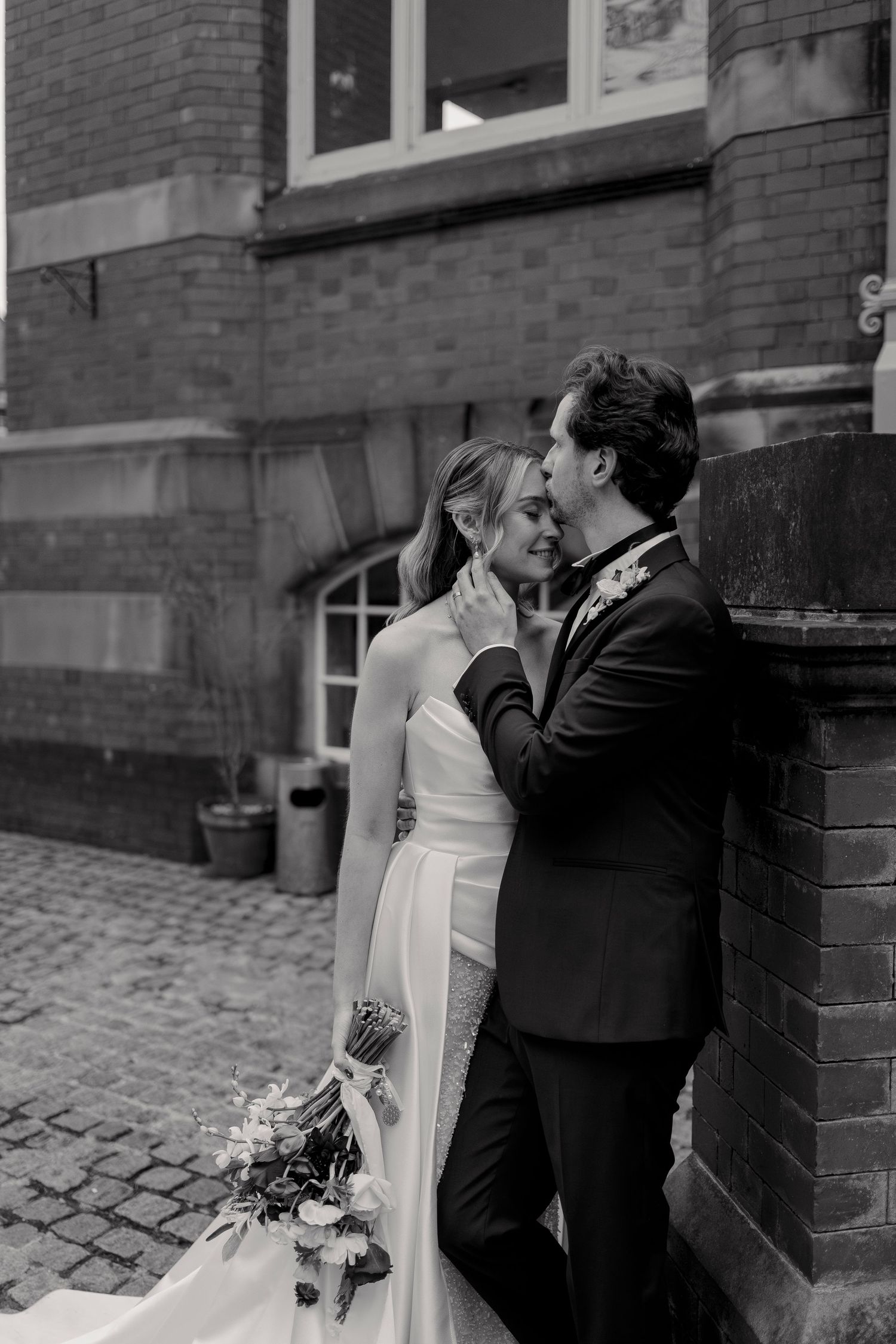 Black and white wedding portraits against brick building with cobblestone street.