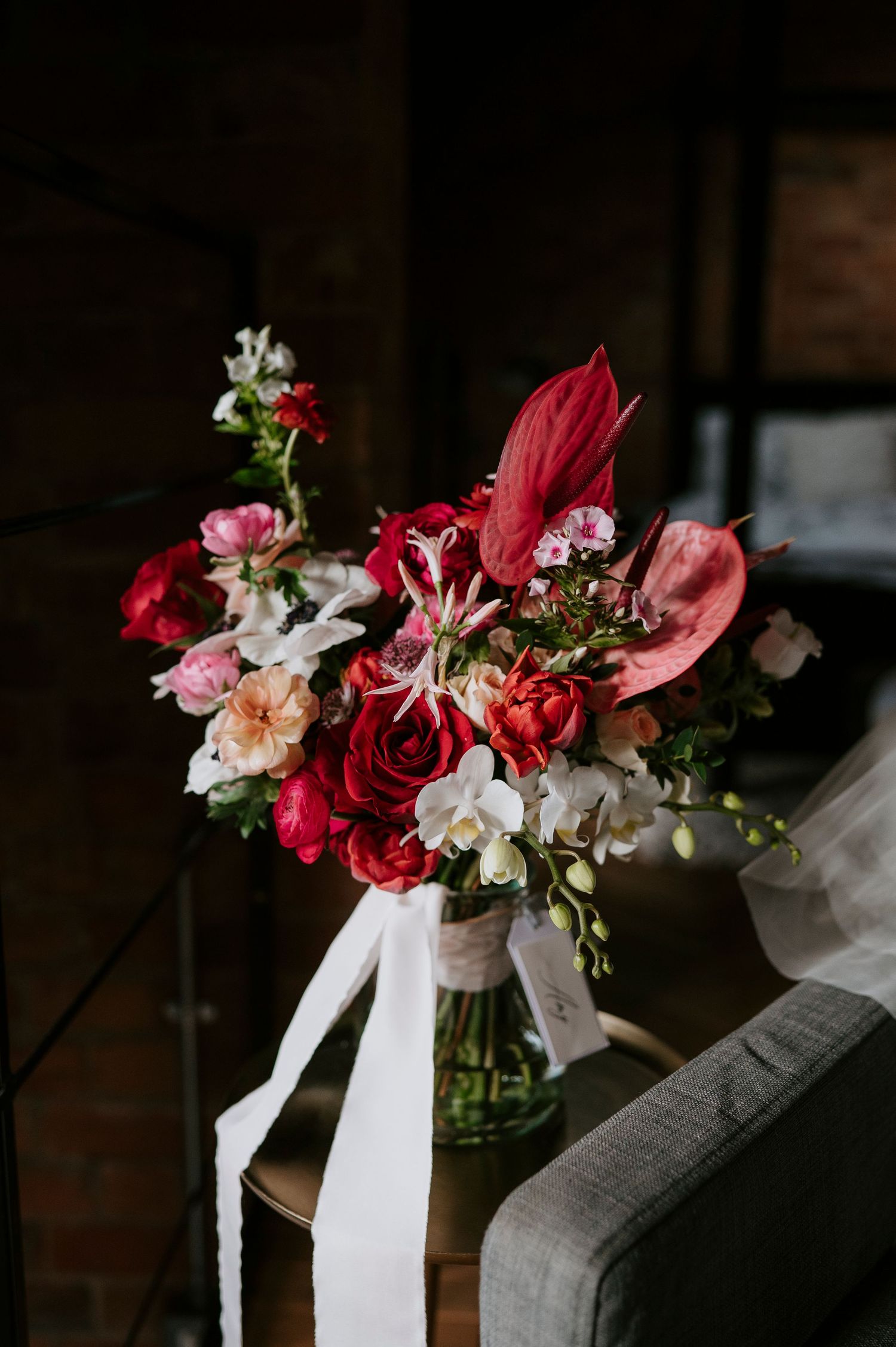 Beautiful floral arrangements with red and pink flowers tied with white ribbons sit on a dark wooden surface.
