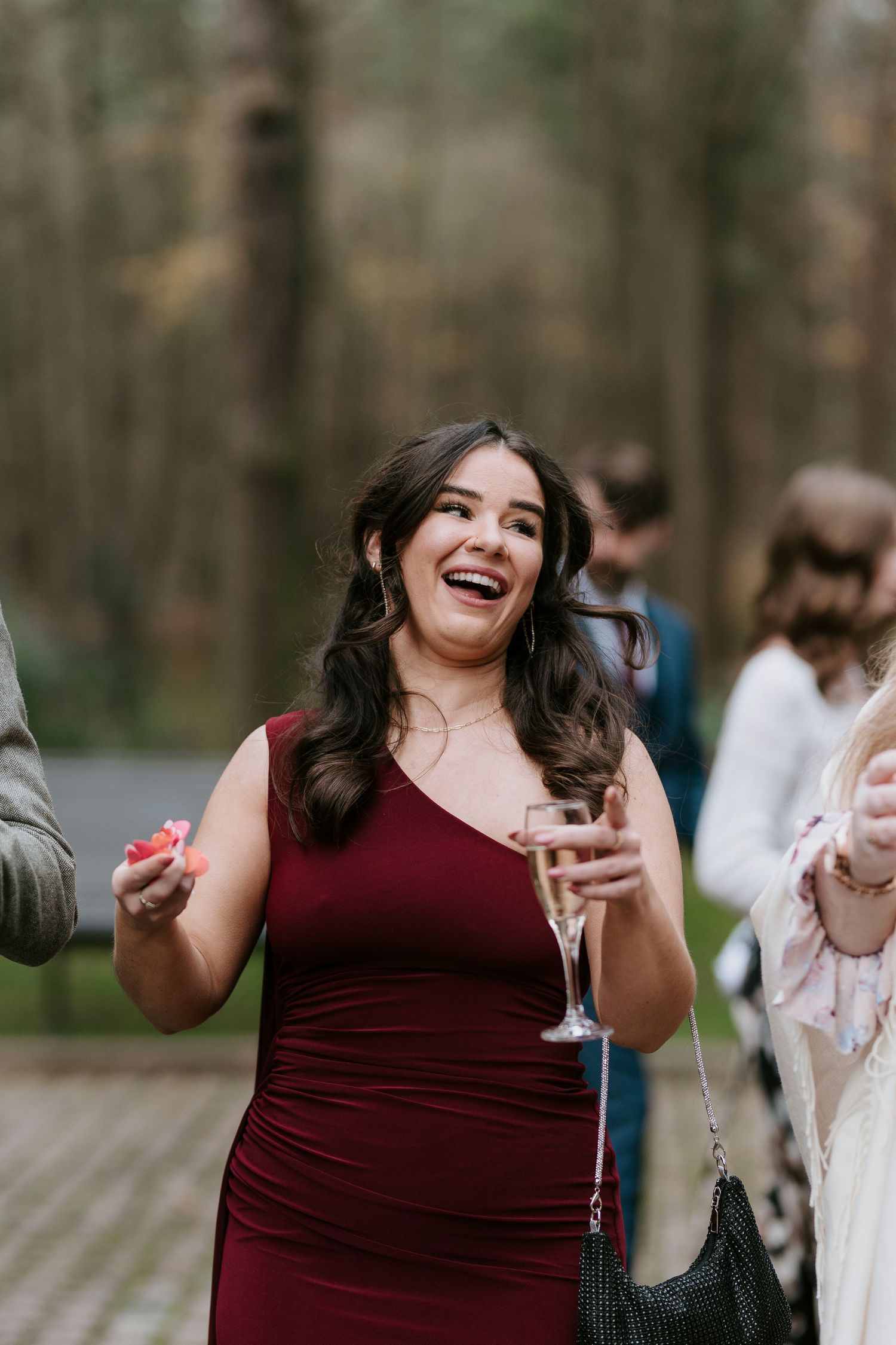 Wedding guest in burgundy dress laughing and enjoying celebration outdoors.