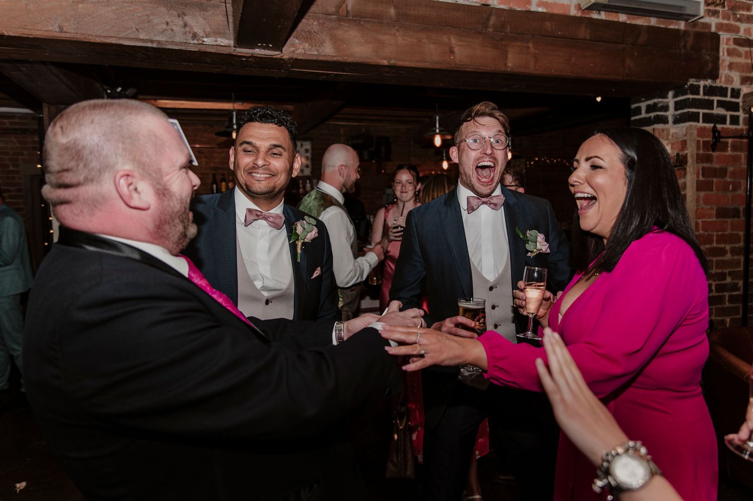 A group of people dancing and celebrating at a wedding reception in a rustic brick-walled venue.