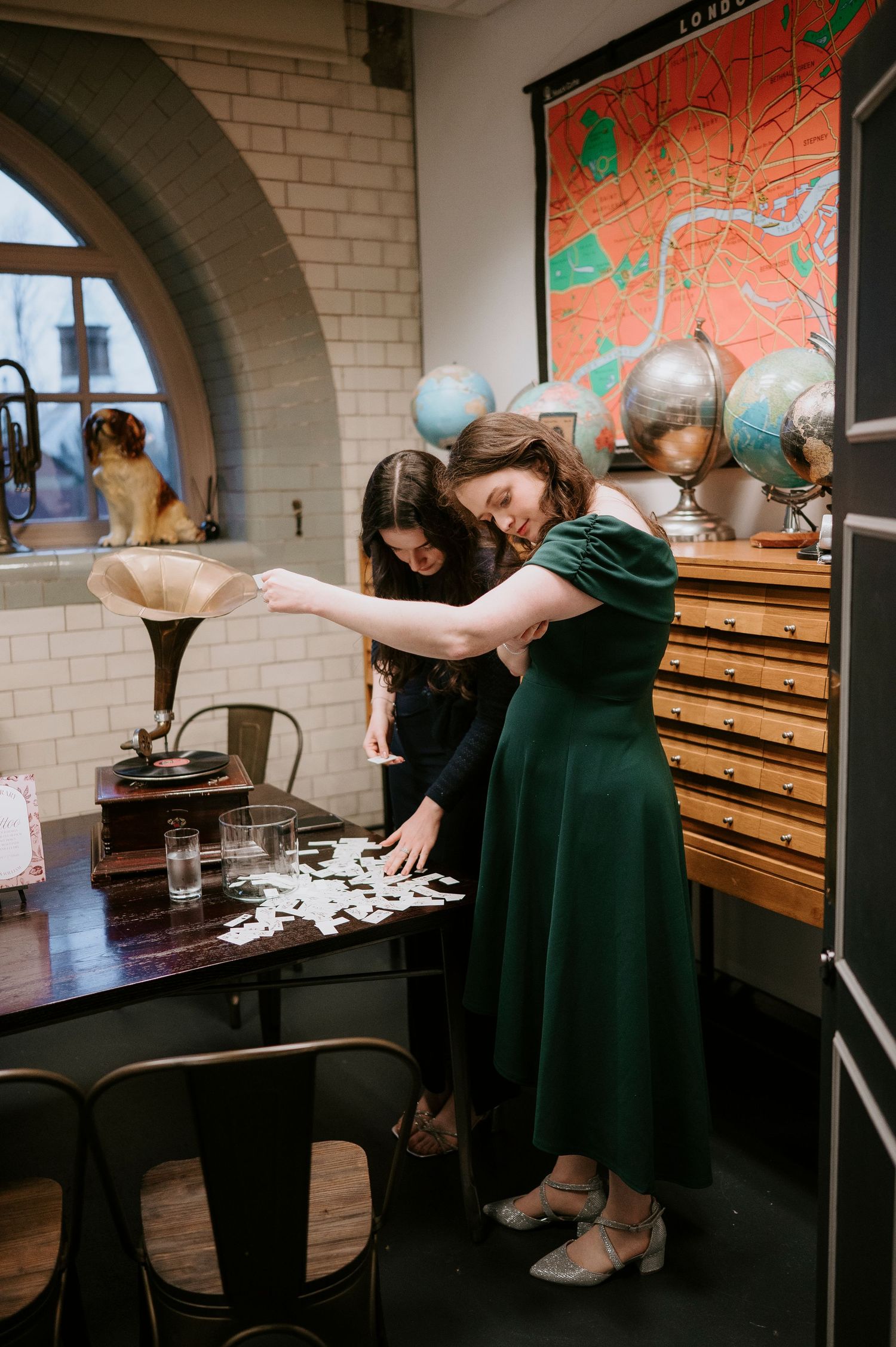 Three sequential photos show someone in a black dress examining items in wooden drawers against a brick wall with artwork.