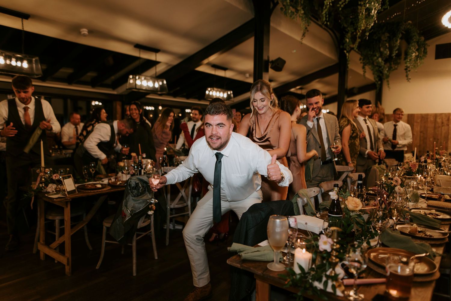Wedding guests celebrating at a reception dinner with rustic decor and greenery garlands.