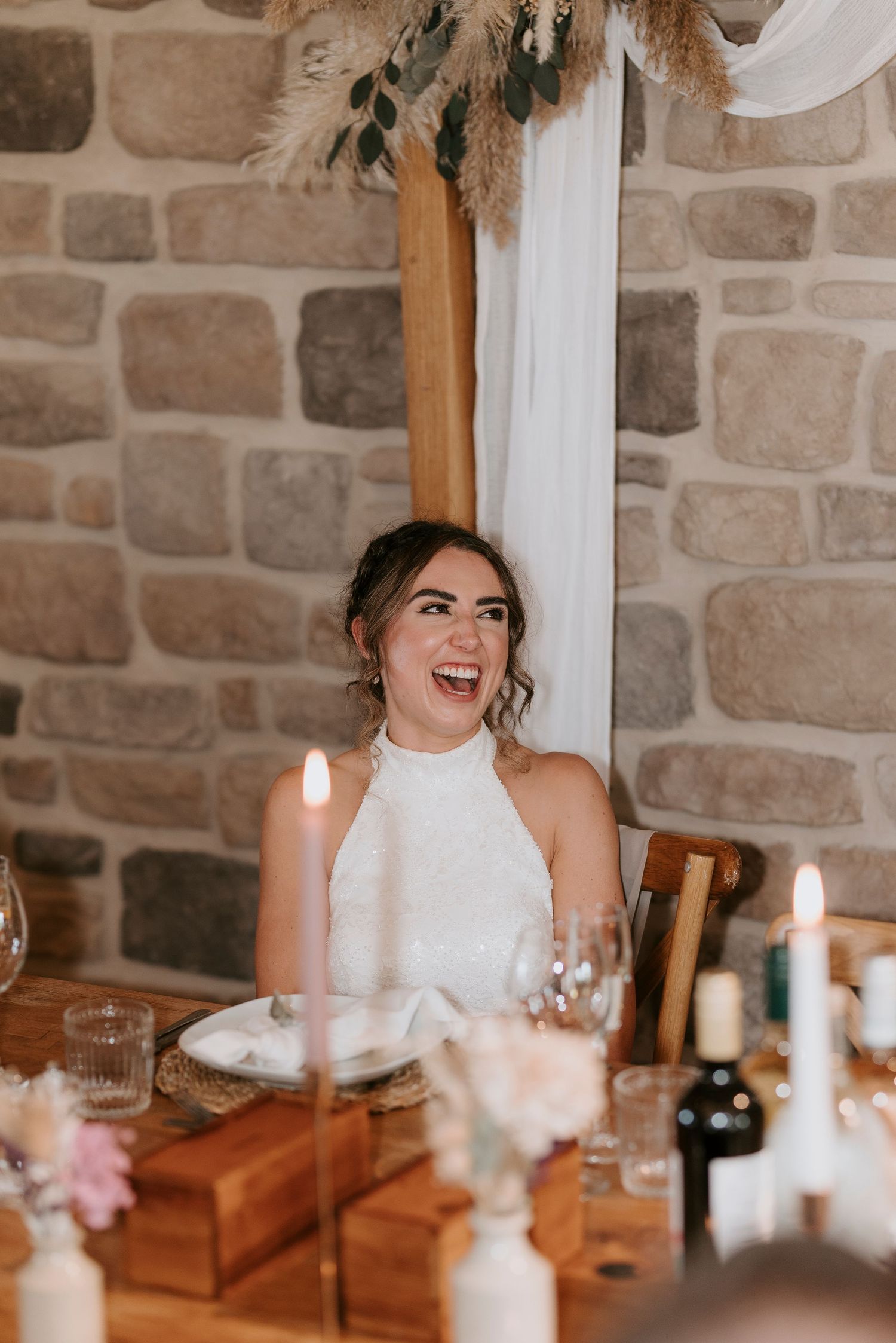 Candid moment of laughter during a wedding reception with stone walls and glowing candles on wooden tables.