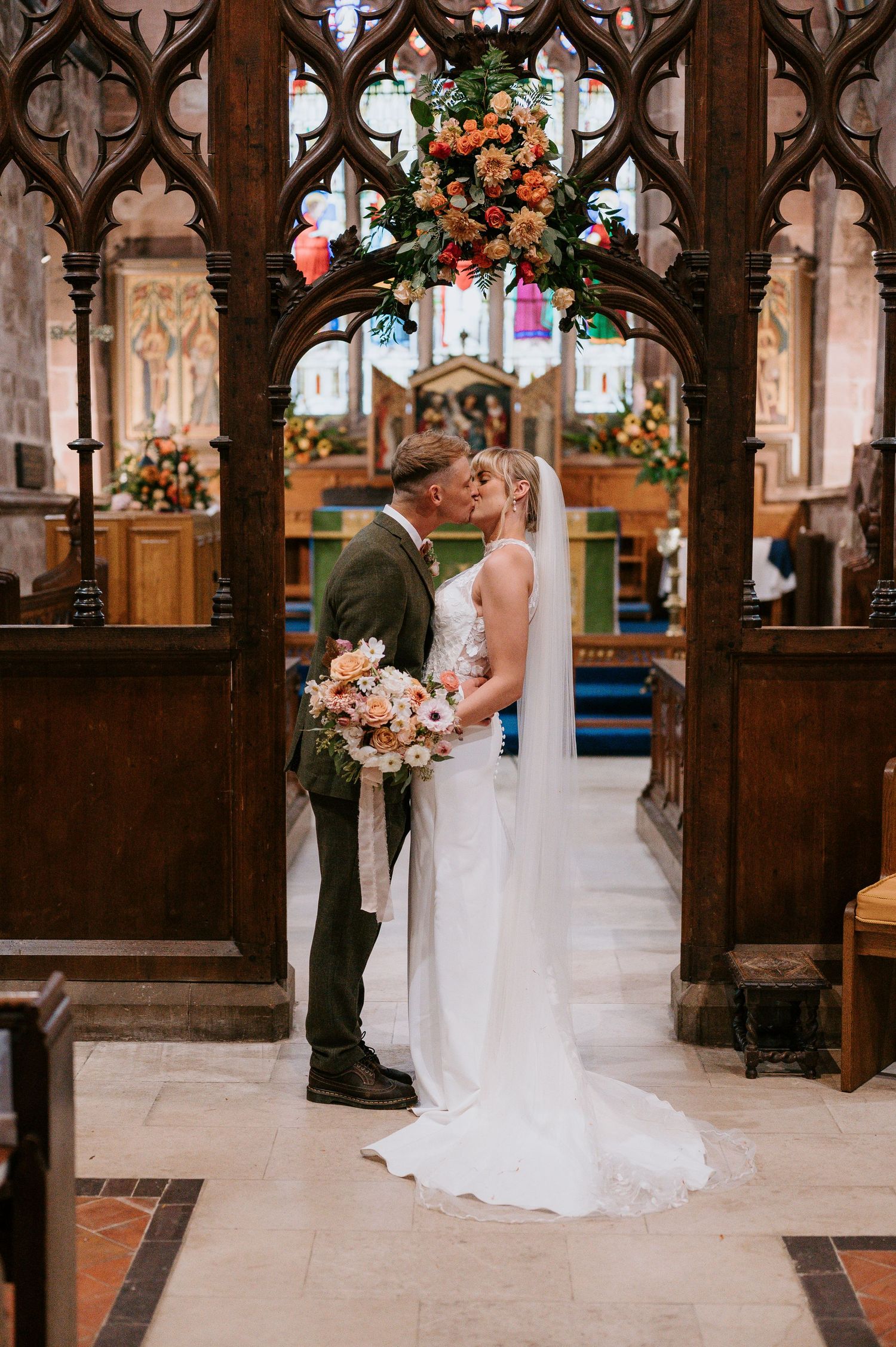 Wedding ceremony takes place in a beautiful gothic church with ornate wooden details and floral arrangements.