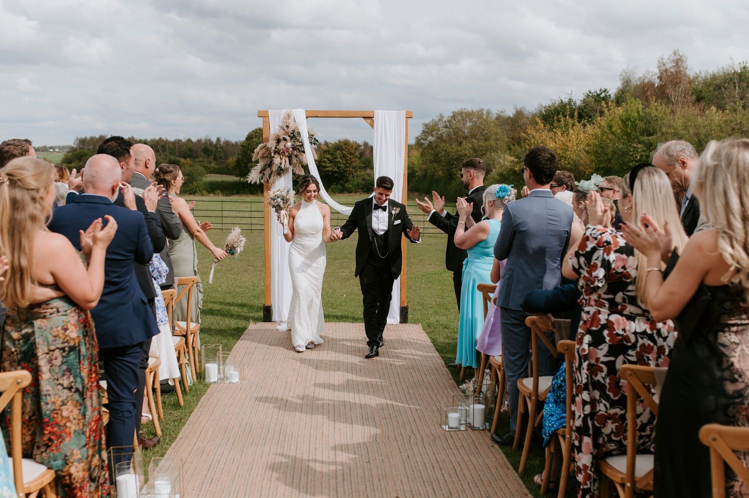 Wedding guests gather outdoors on a sunny day to celebrate during a rustic countryside ceremony.