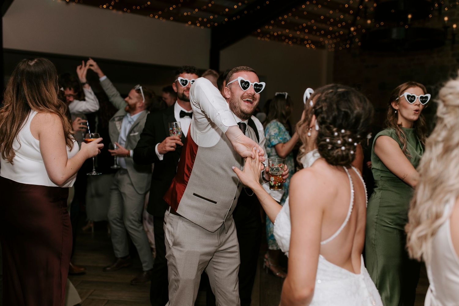 Wedding guests dance and celebrate on a dimly lit dance floor during an evening reception party.