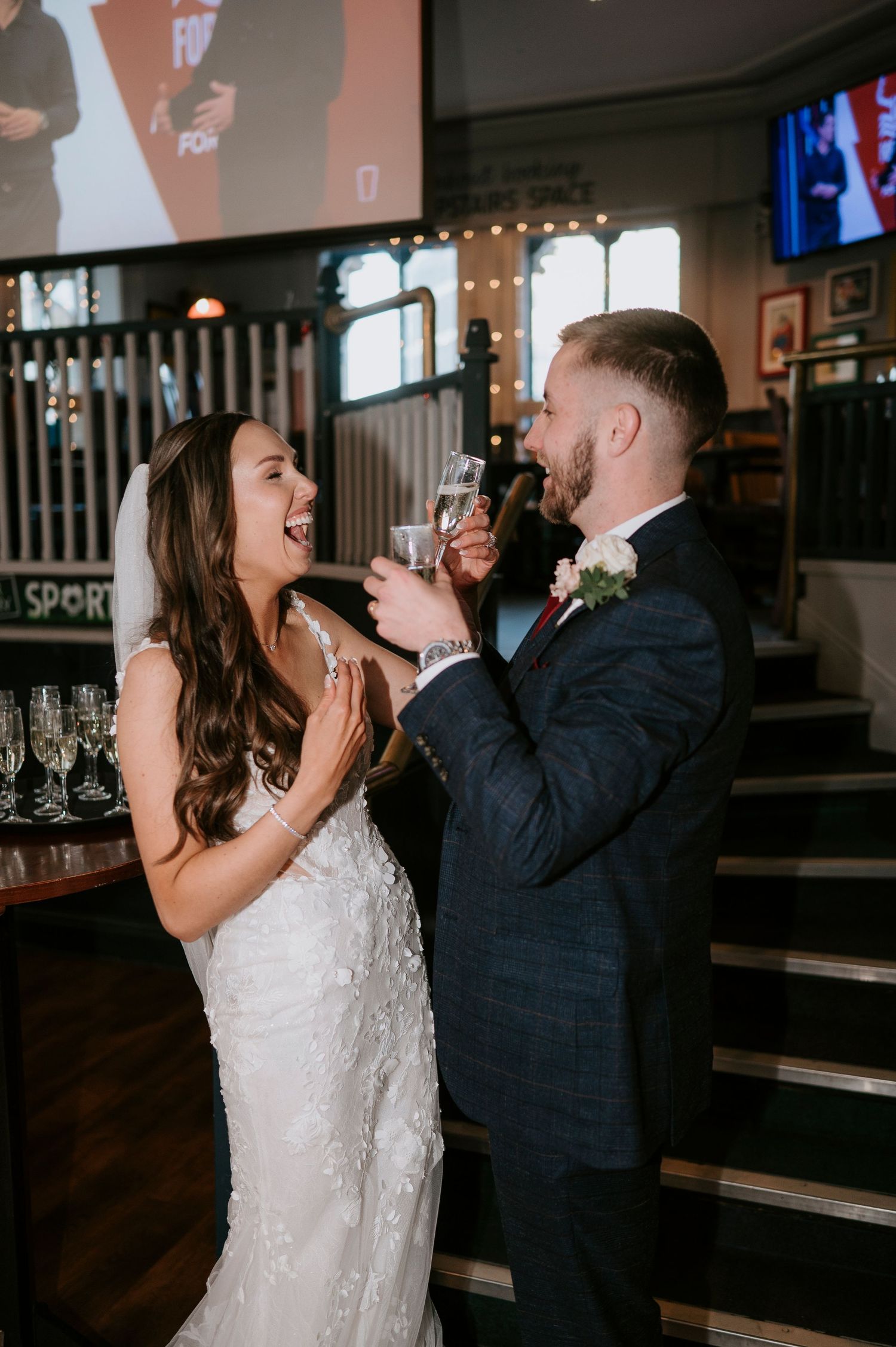 Bride and groom toast champagne glasses indoors at wedding reception venue, smiling joyfully.